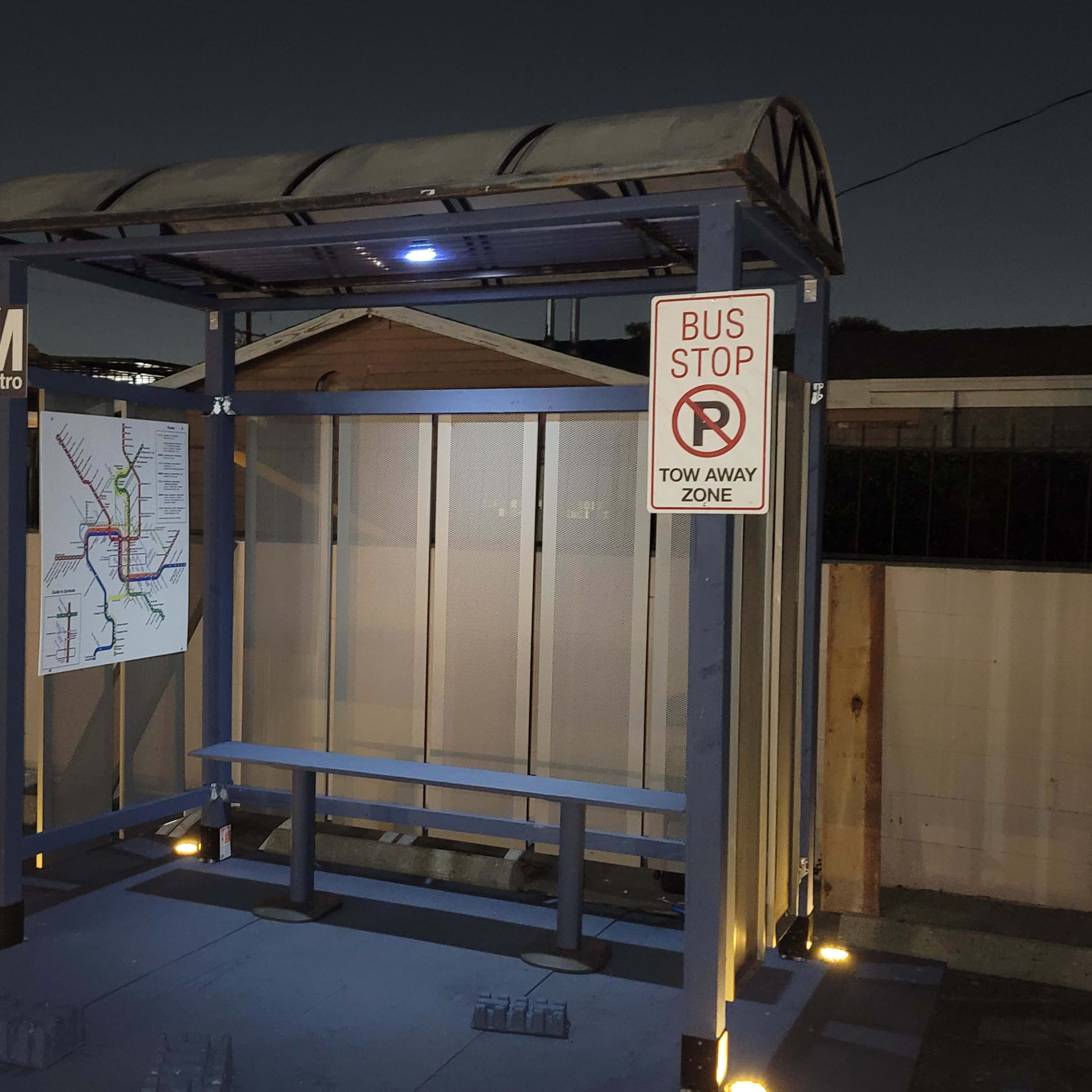 A bus stop shelter with a map and signage is illuminated at night.