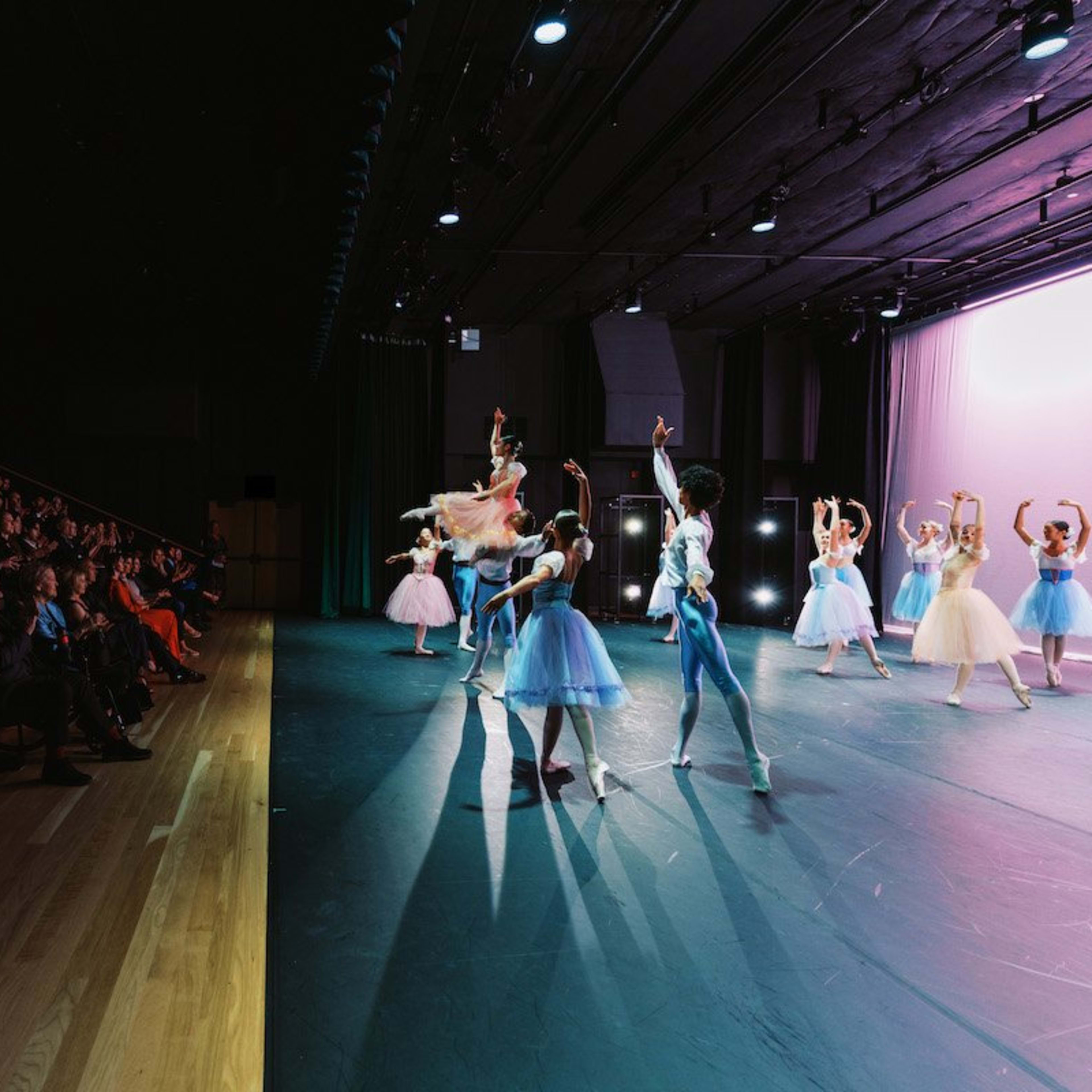 A ballet performance takes place on stage while an audience watches from a seated area.