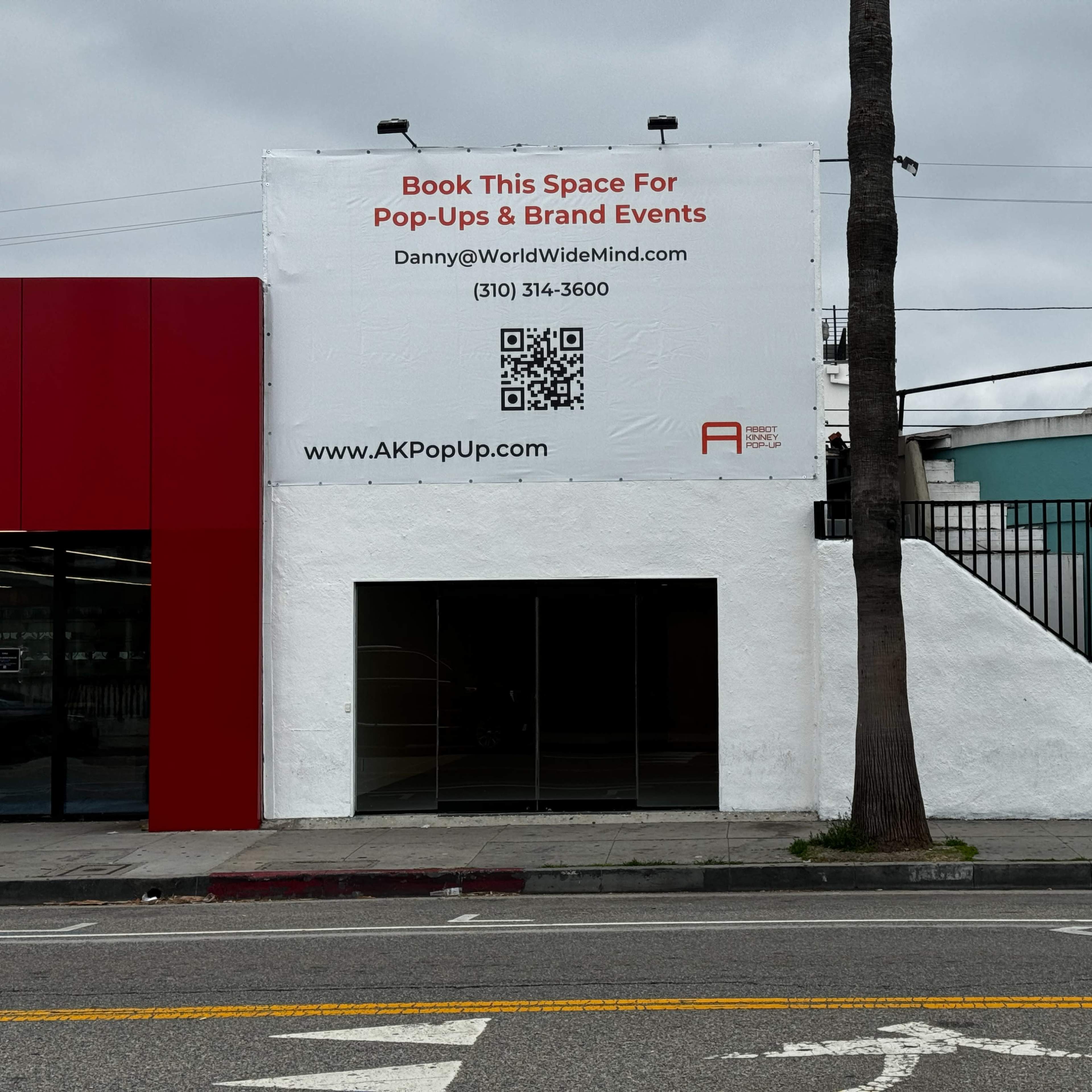 A building with a white exterior features a large sign advertising booking space for pop-ups and brand events, along with contact information and a QR code.