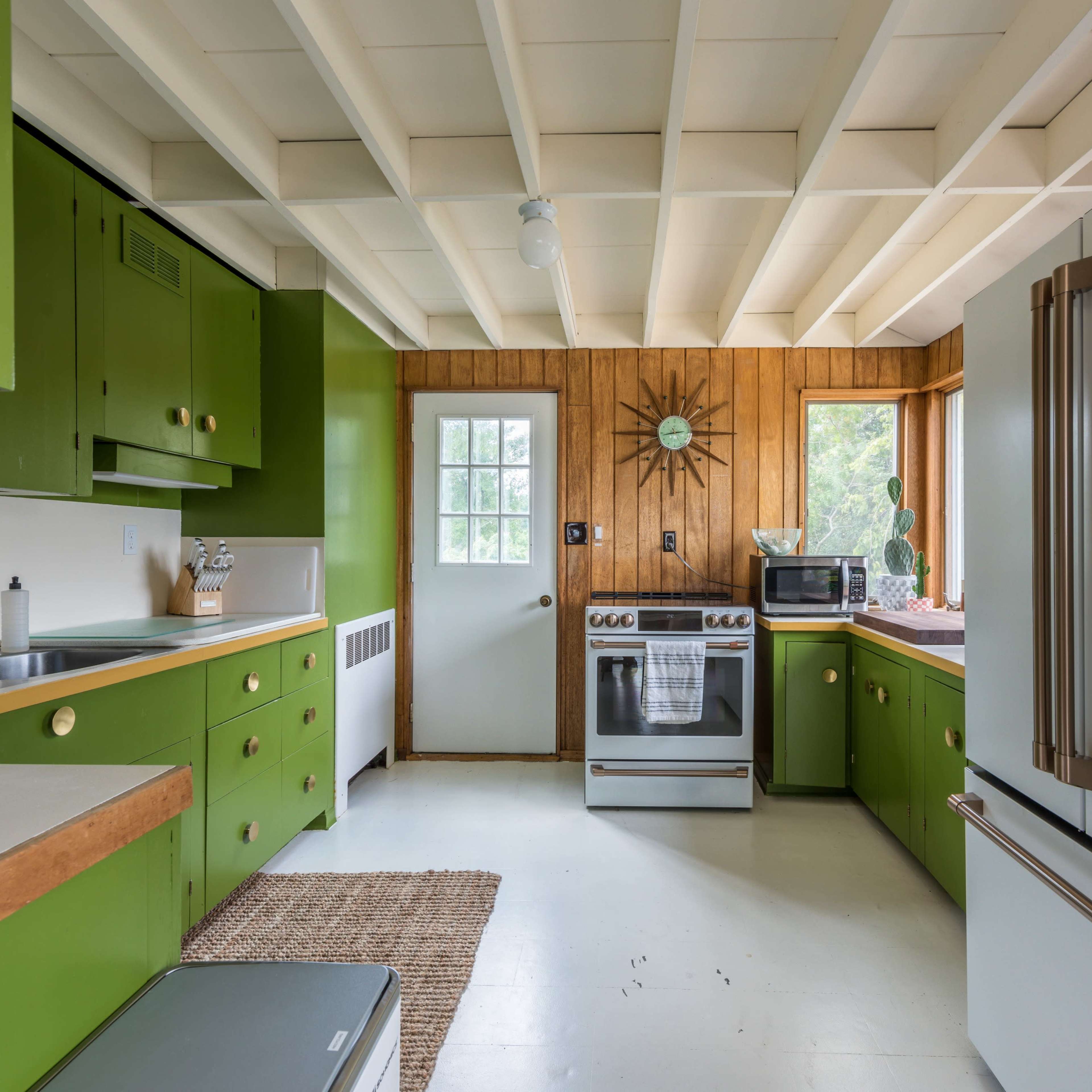 The kitchen features green cabinets, a white stove and refrigerator, and a wood-paneled wall with a window.
