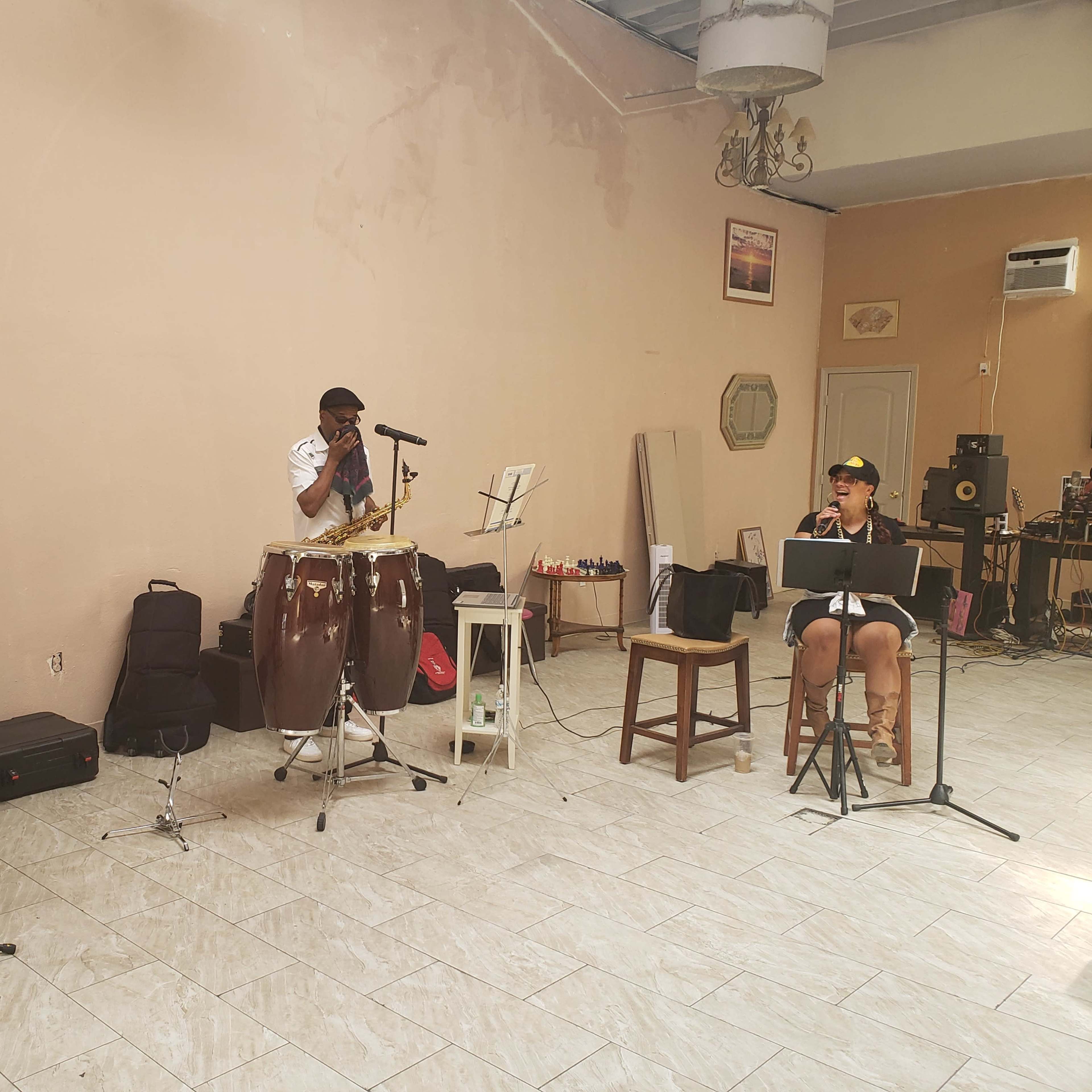 Three musicians perform in a spacious room filled with instruments and sound equipment.