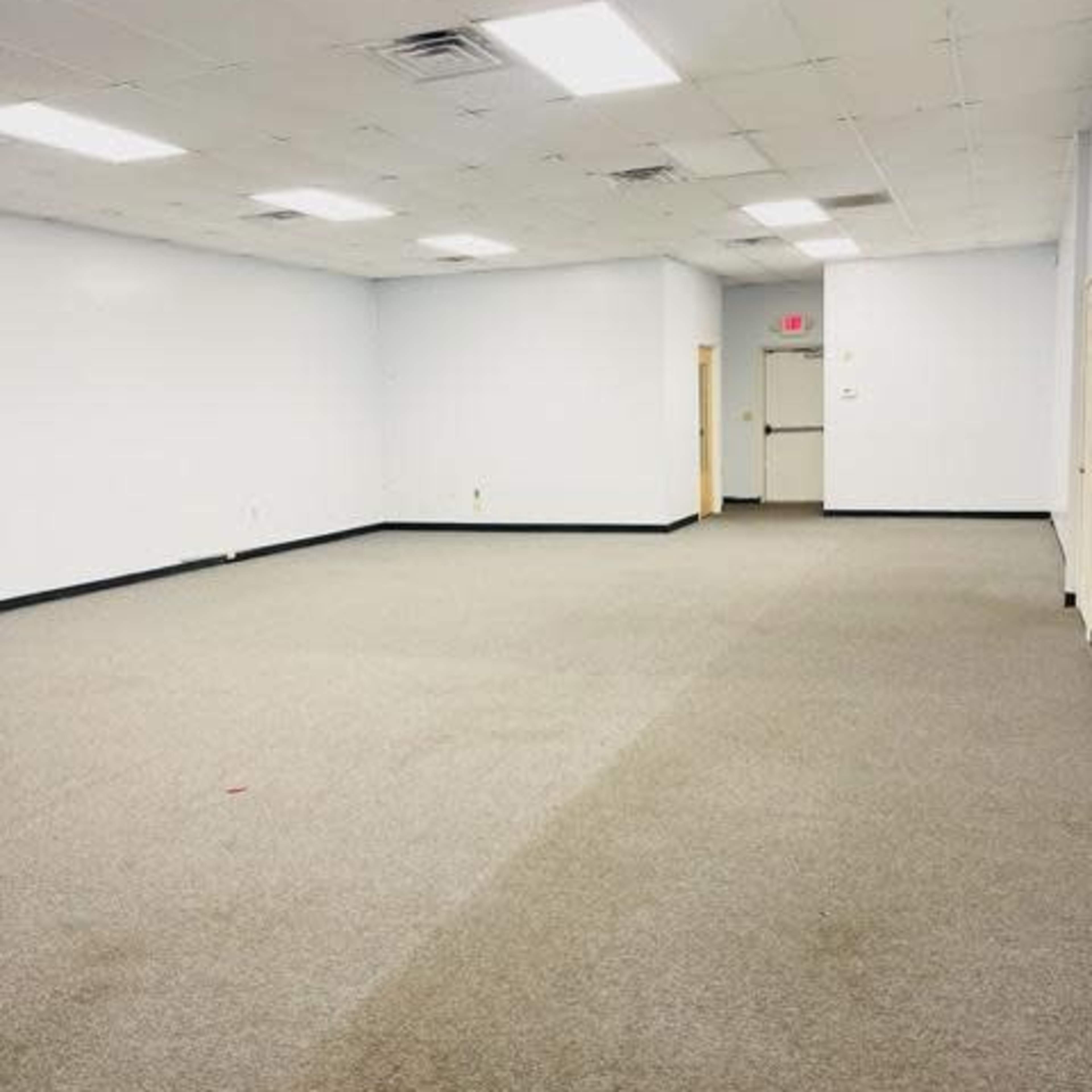 A large, empty room with gray carpeting and fluorescent lighting.