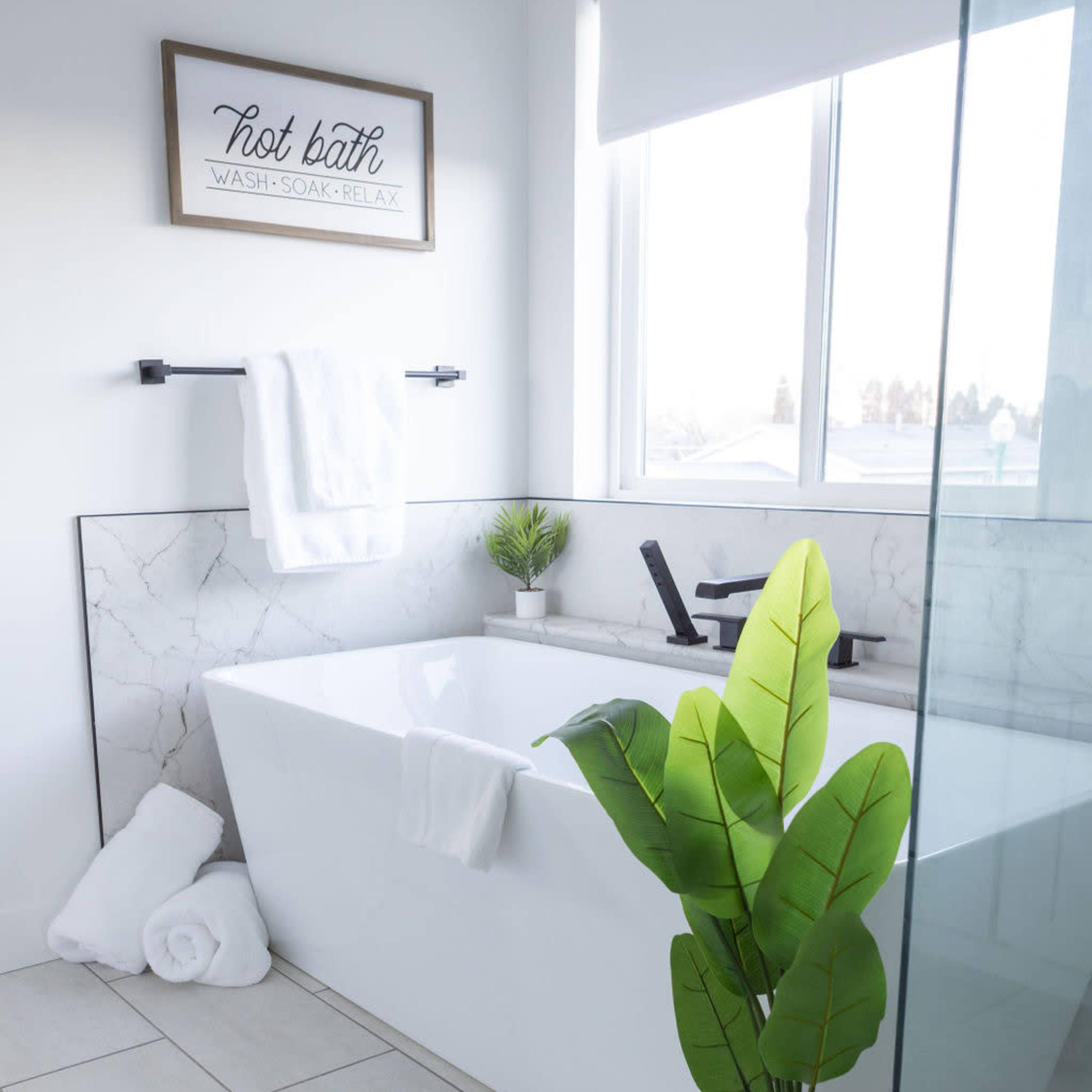 A modern bathroom featuring a freestanding bathtub, a glass shower enclosure, white towels hanging on a bar, and a potted plant beside the tub.