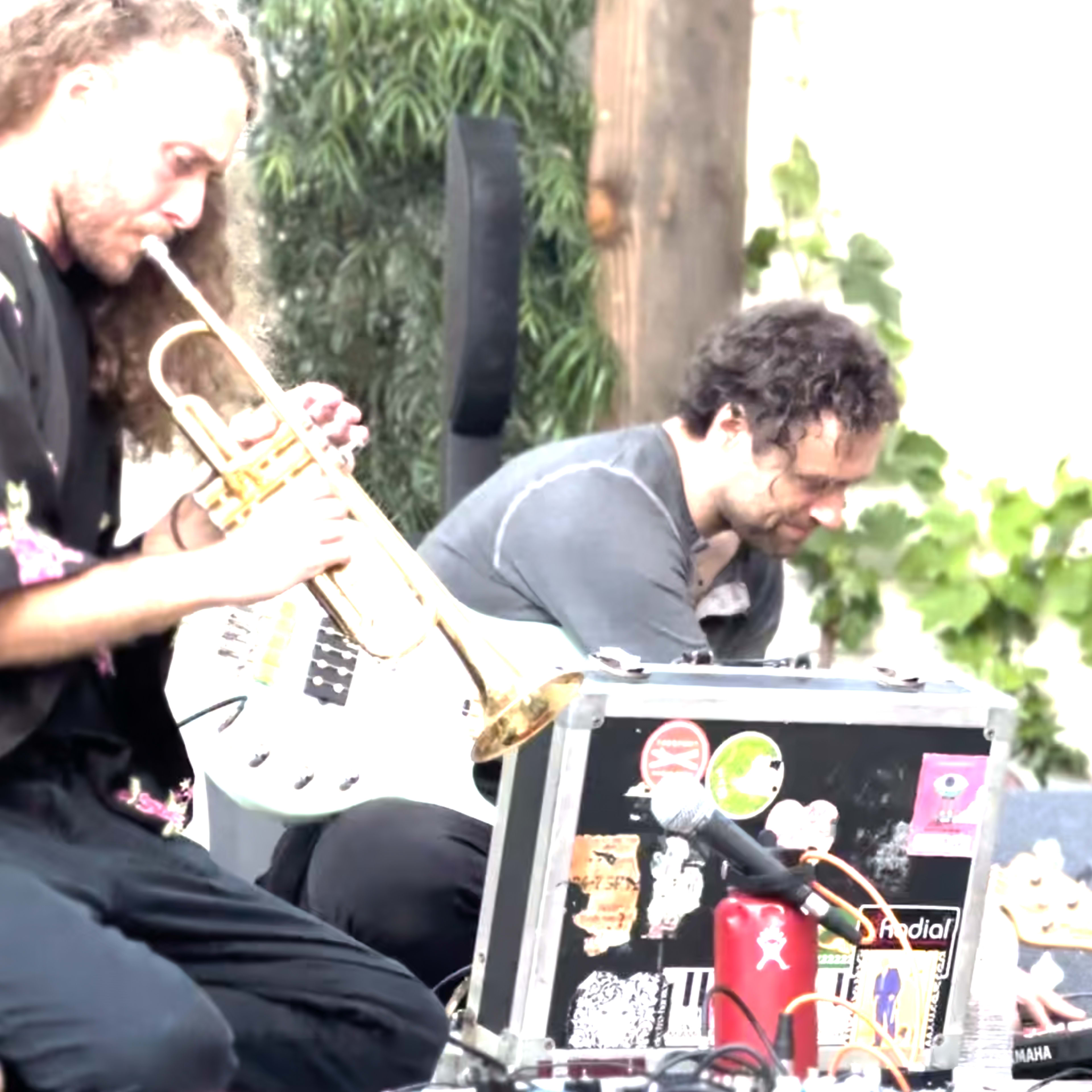 Two musicians perform on stage, one playing a trumpet and the other manipulating electronic equipment.