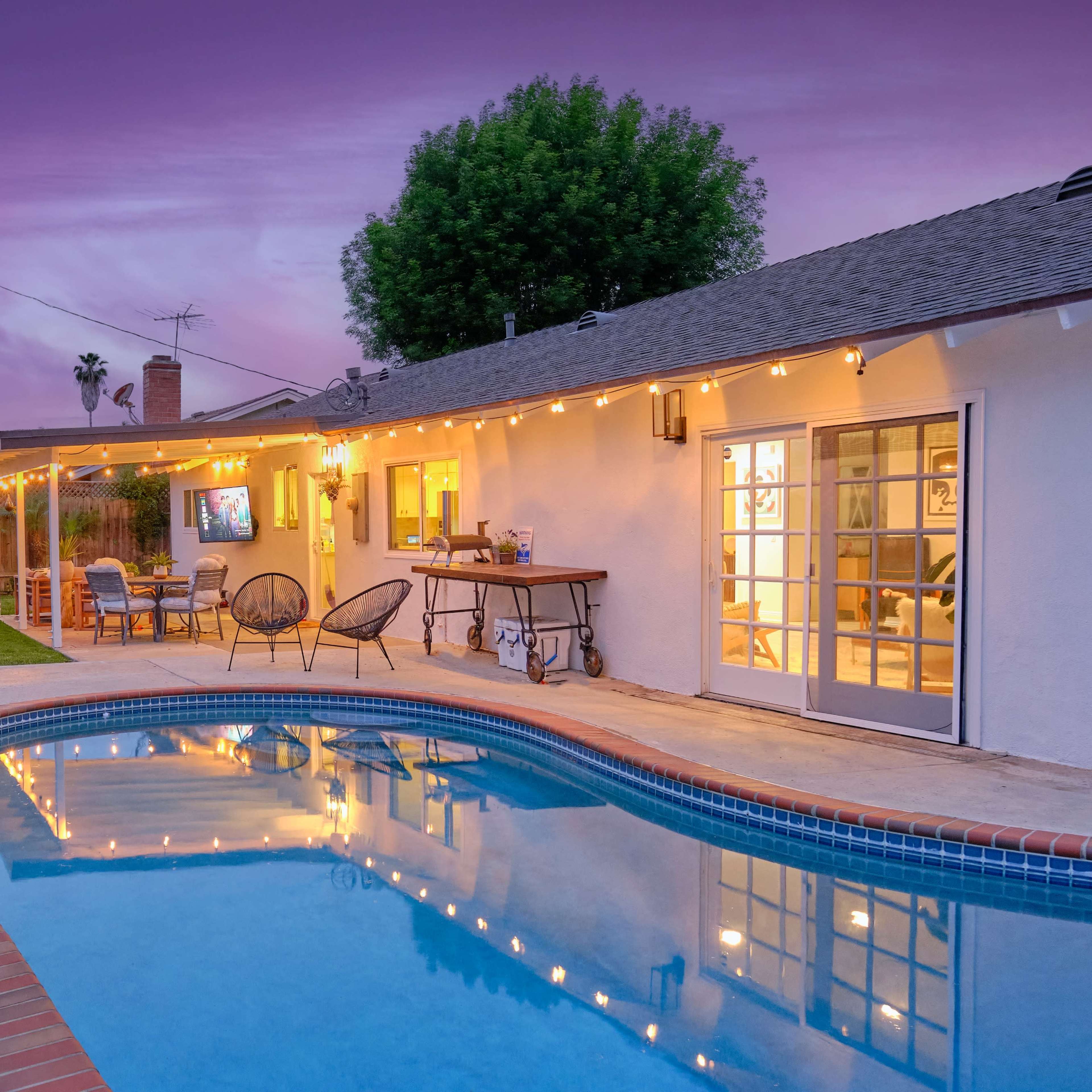 A backyard pool with colorful string lights and a well-maintained patio area at dusk.