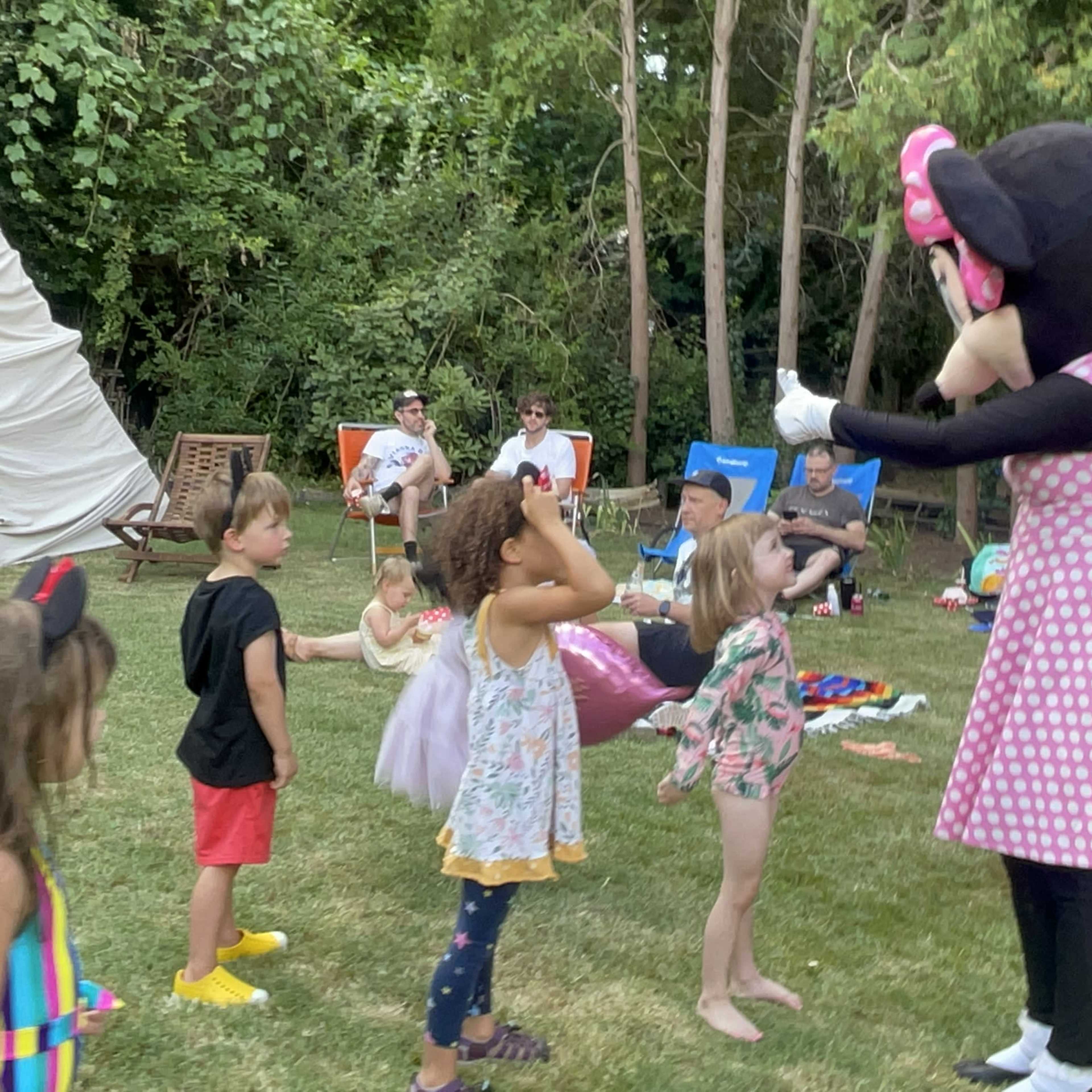 A costumed character resembling a mouse engages with a group of children in a backyard setting.