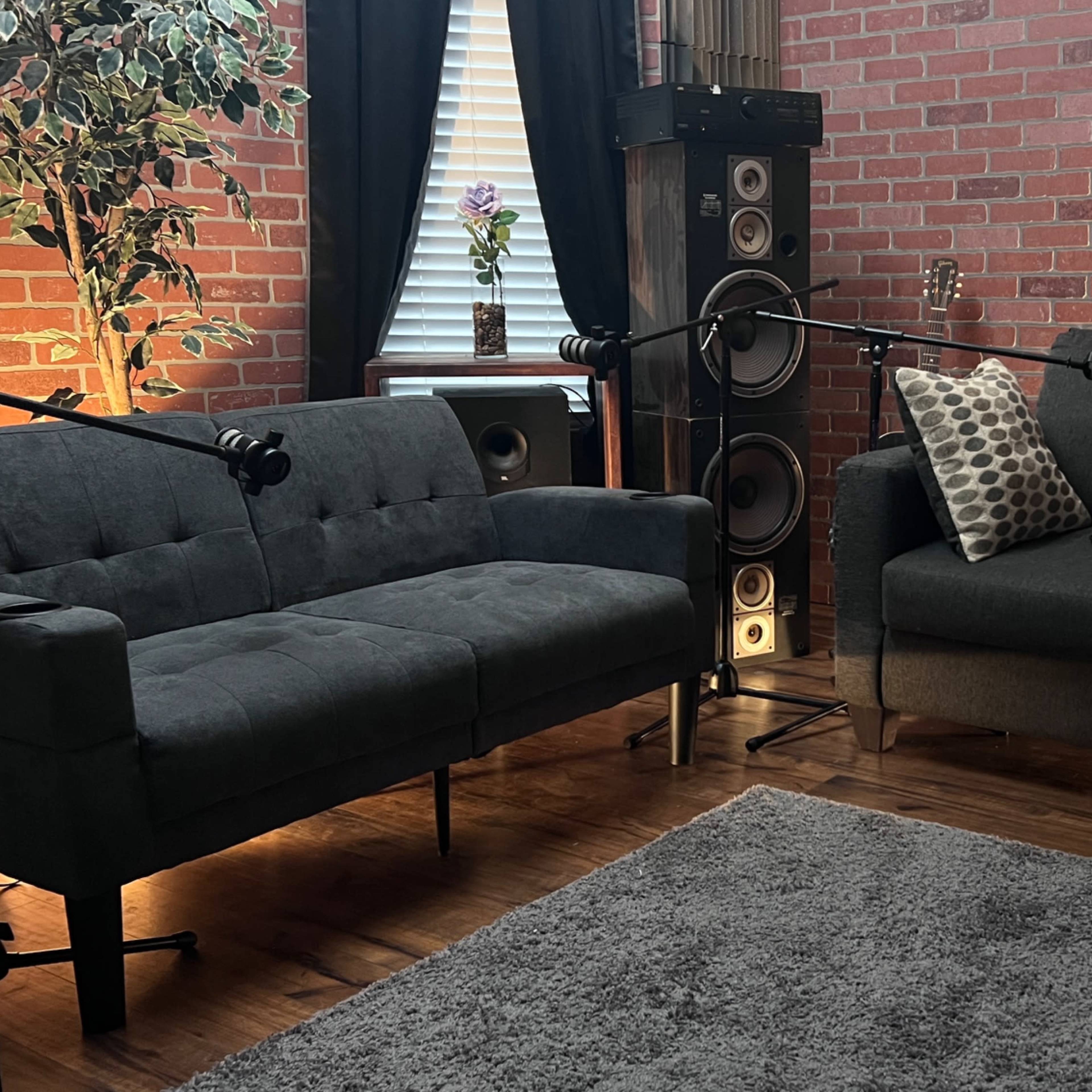 A cozy living room with two dark gray sofas, a rug, and audio equipment, illuminated by soft lighting.