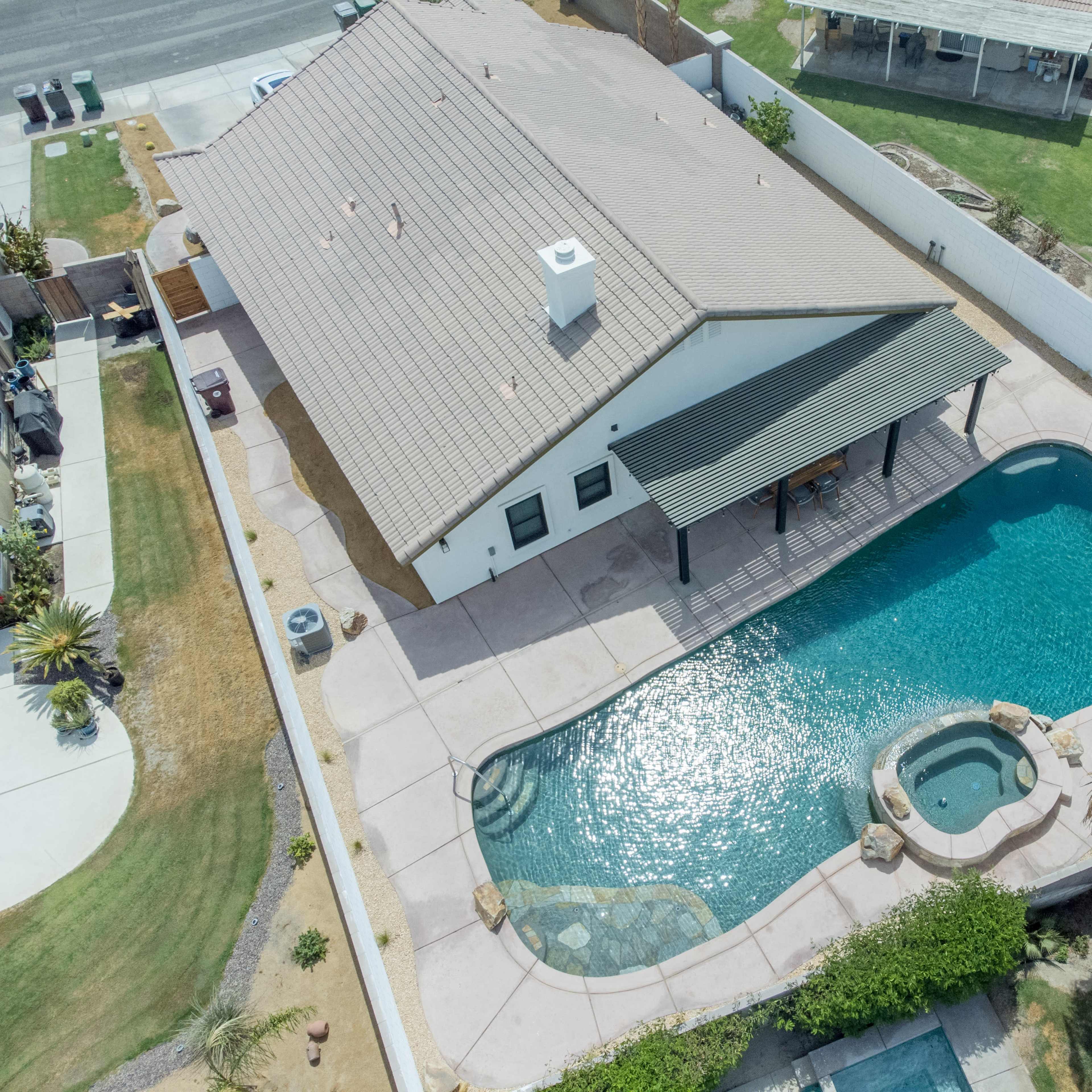 An aerial view shows a house with a pool and spa in the backyard, surrounded by a fence and landscaped areas.