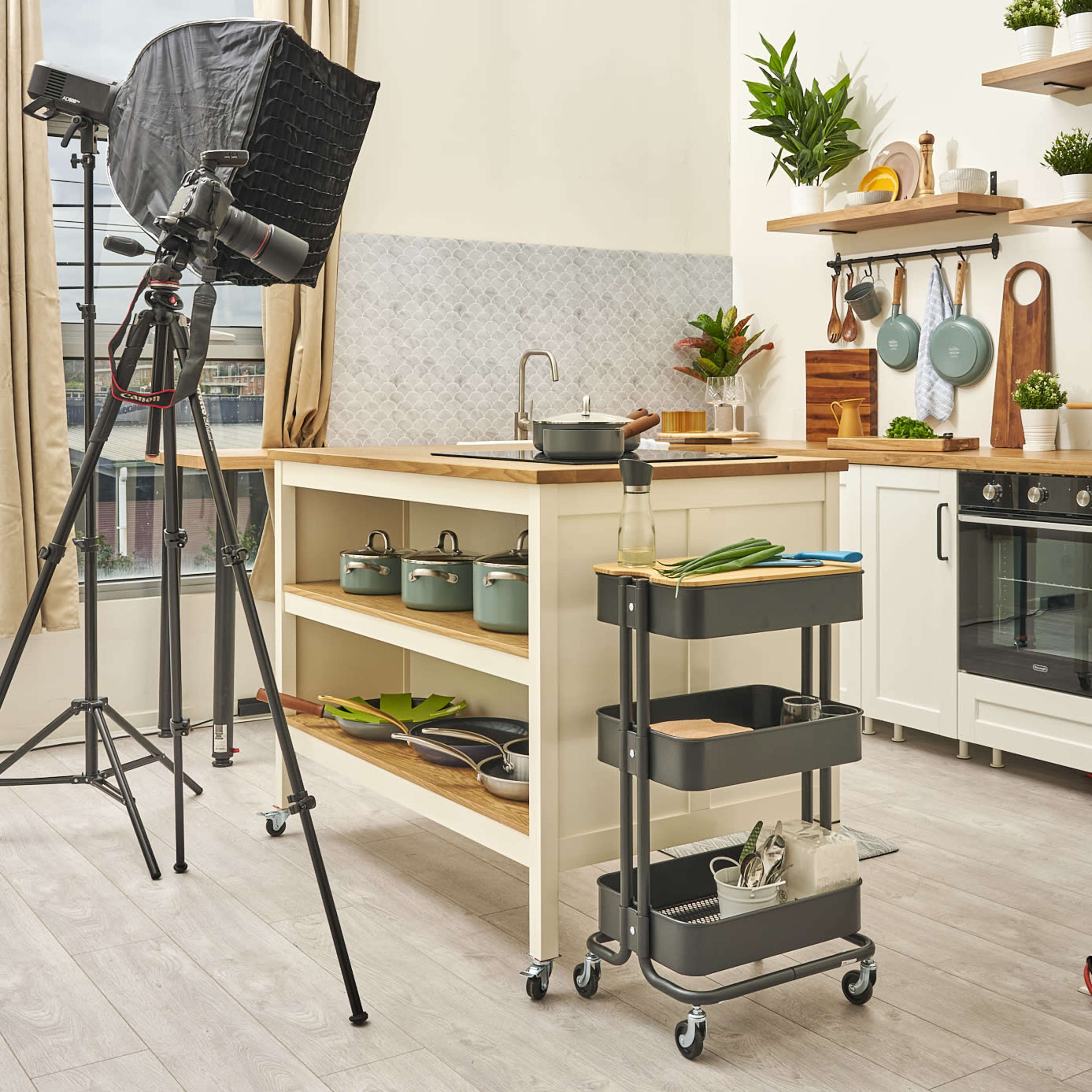 A well-lit kitchen scene features a wooden island with cooking utensils and plants, accompanied by a camera setup on a tripod for filming.