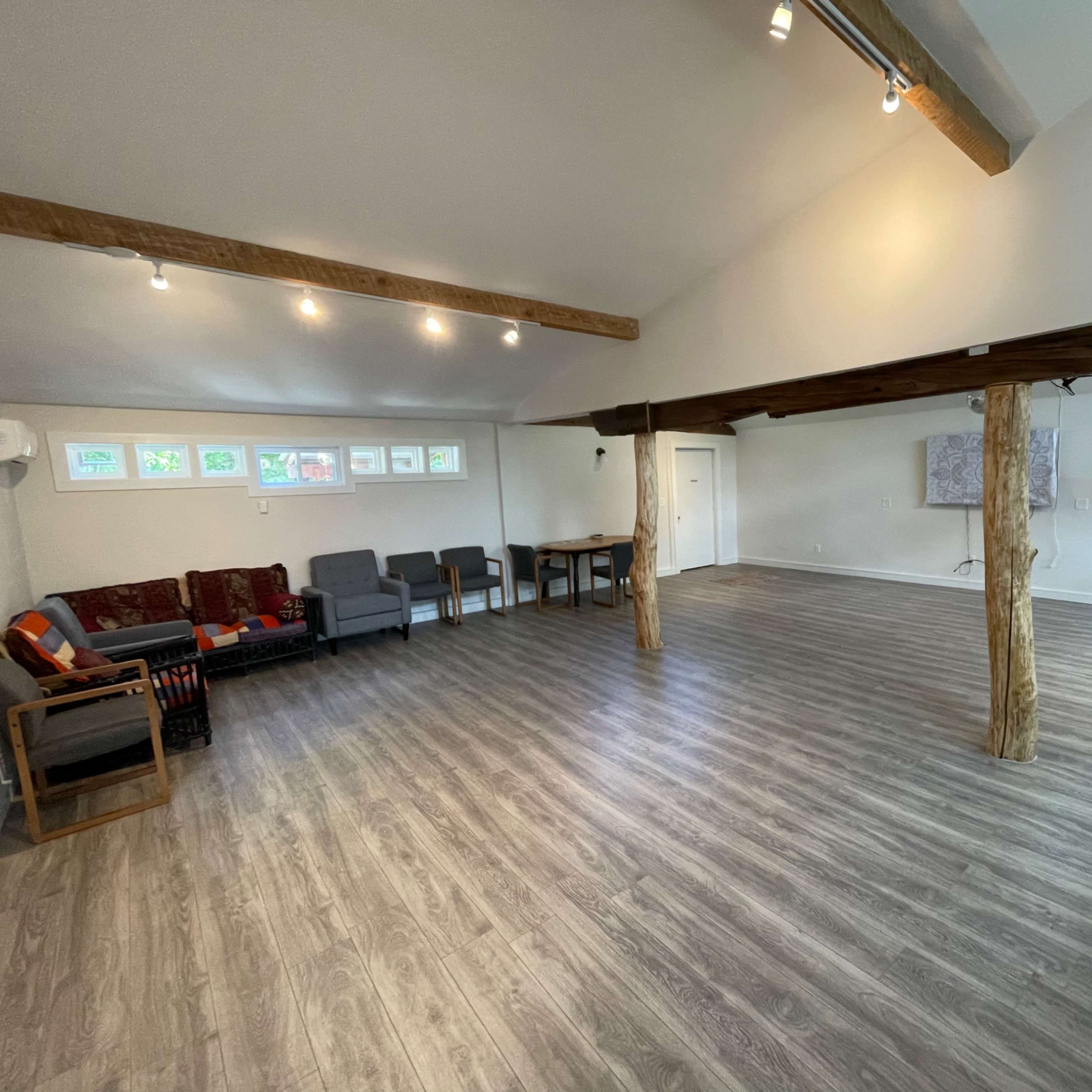 A spacious, well-lit interior with wooden beams, seating areas, and a wooden table in a minimalist design.