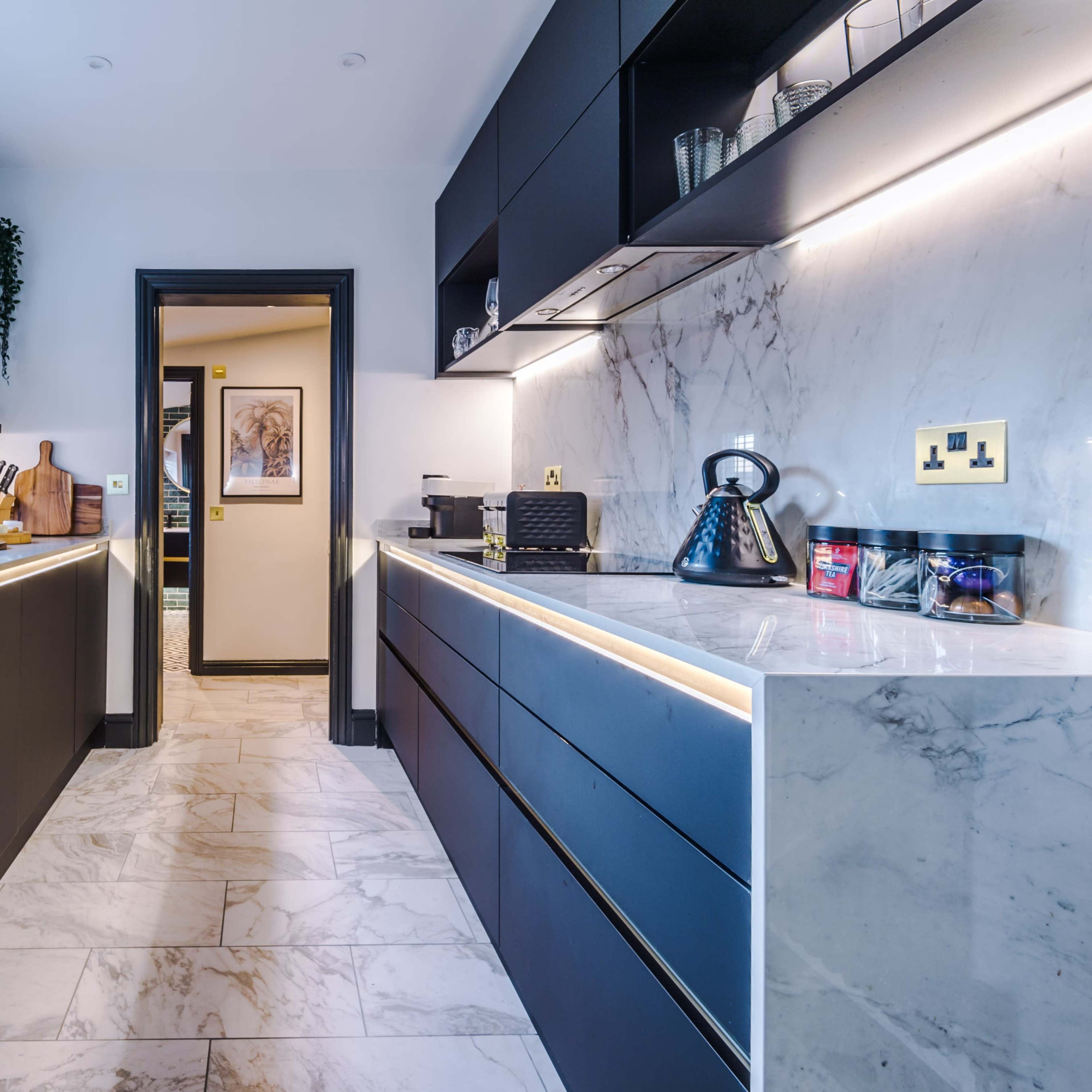 A modern kitchen features black cabinetry, marble countertops, and under-cabinet lighting, creating a sleek and functional space.