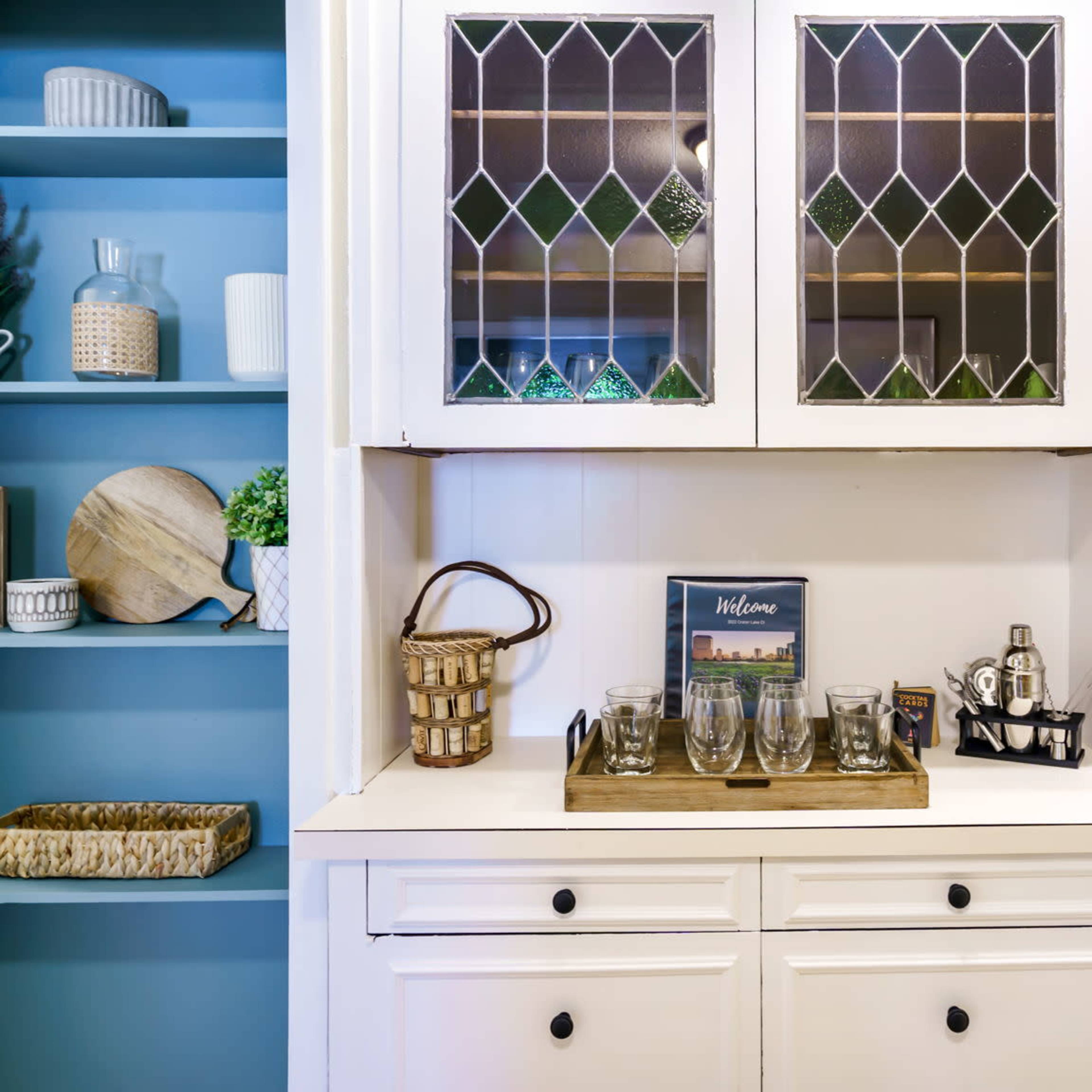 A white cabinet with glass panes is flanked by blue shelves displaying various decorative items and a welcome sign.