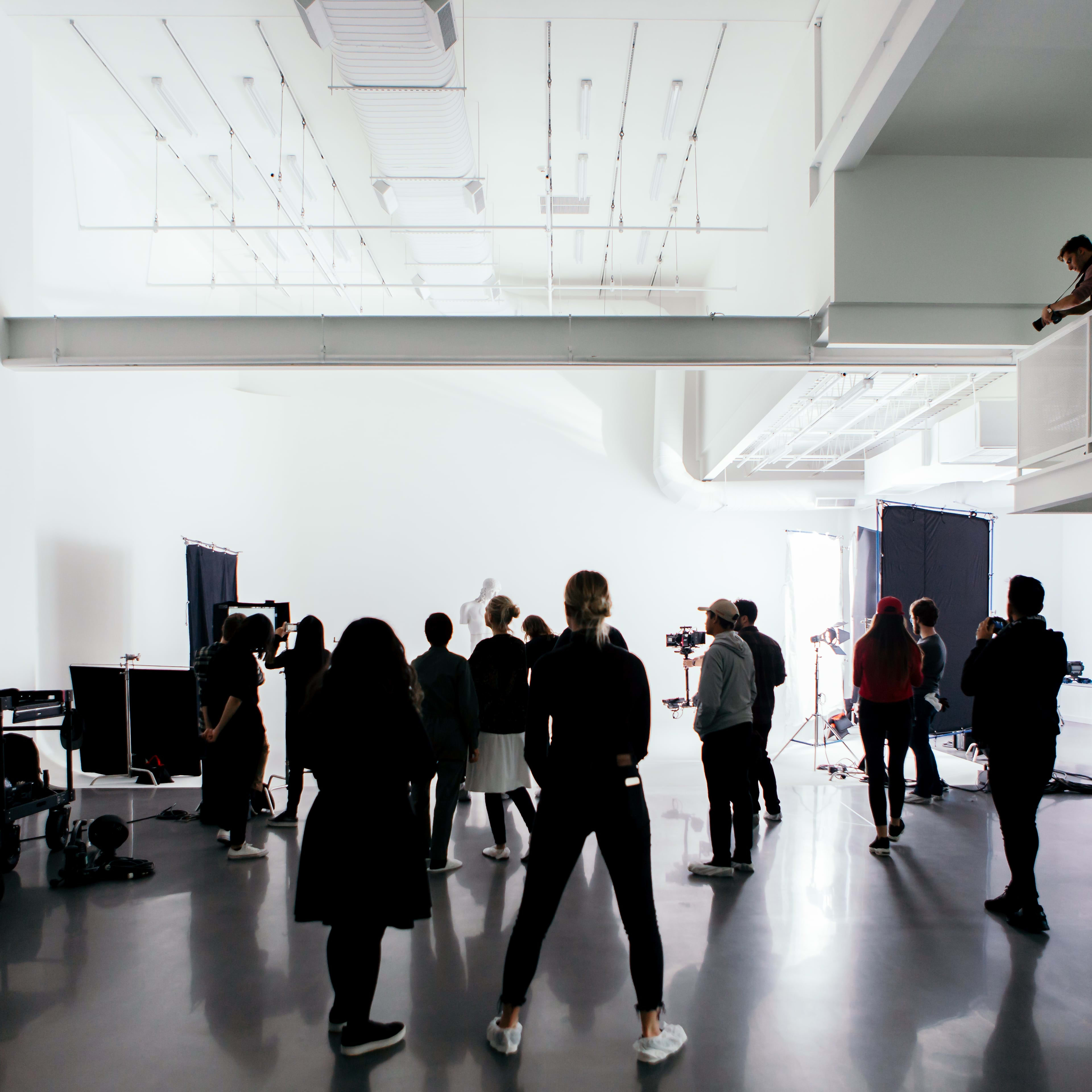 A group of people is gathered in a spacious studio with lighting equipment set up for a photoshoot.