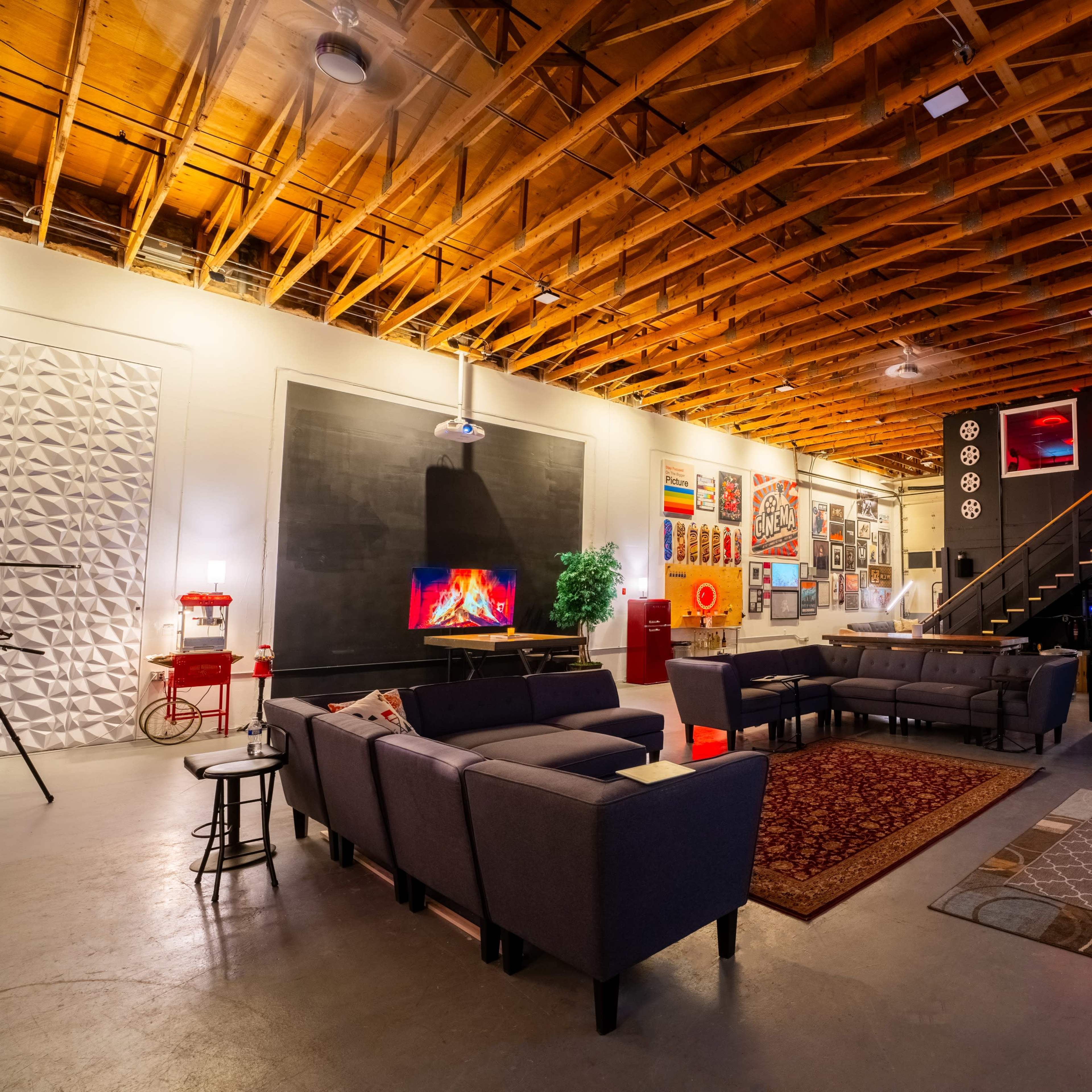 A spacious living room with a high wooden ceiling, modern furniture, and a large wall displaying a projector screen.