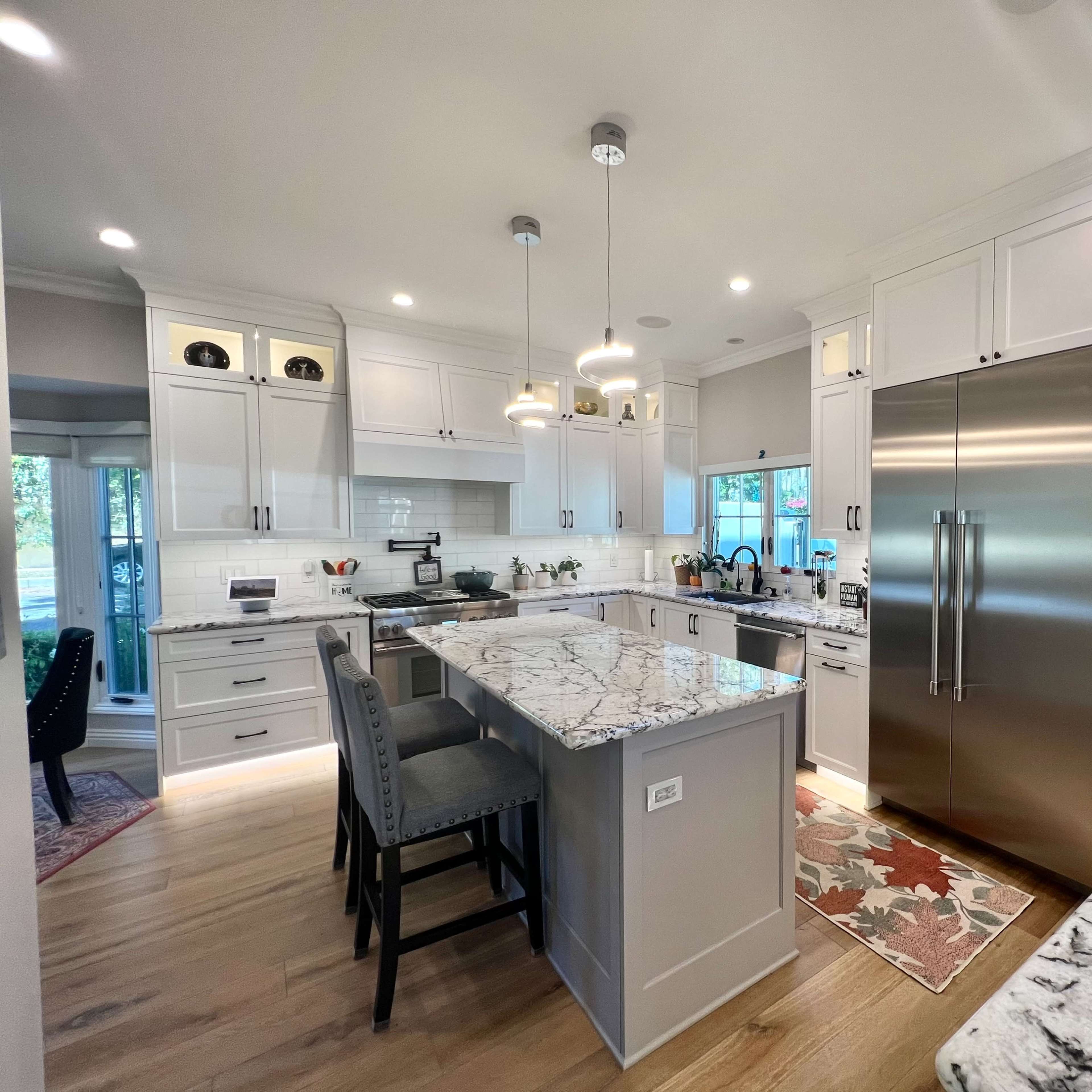 A modern kitchen featuring white cabinetry, a large island with seating, and stainless steel appliances, including a double door refrigerator.