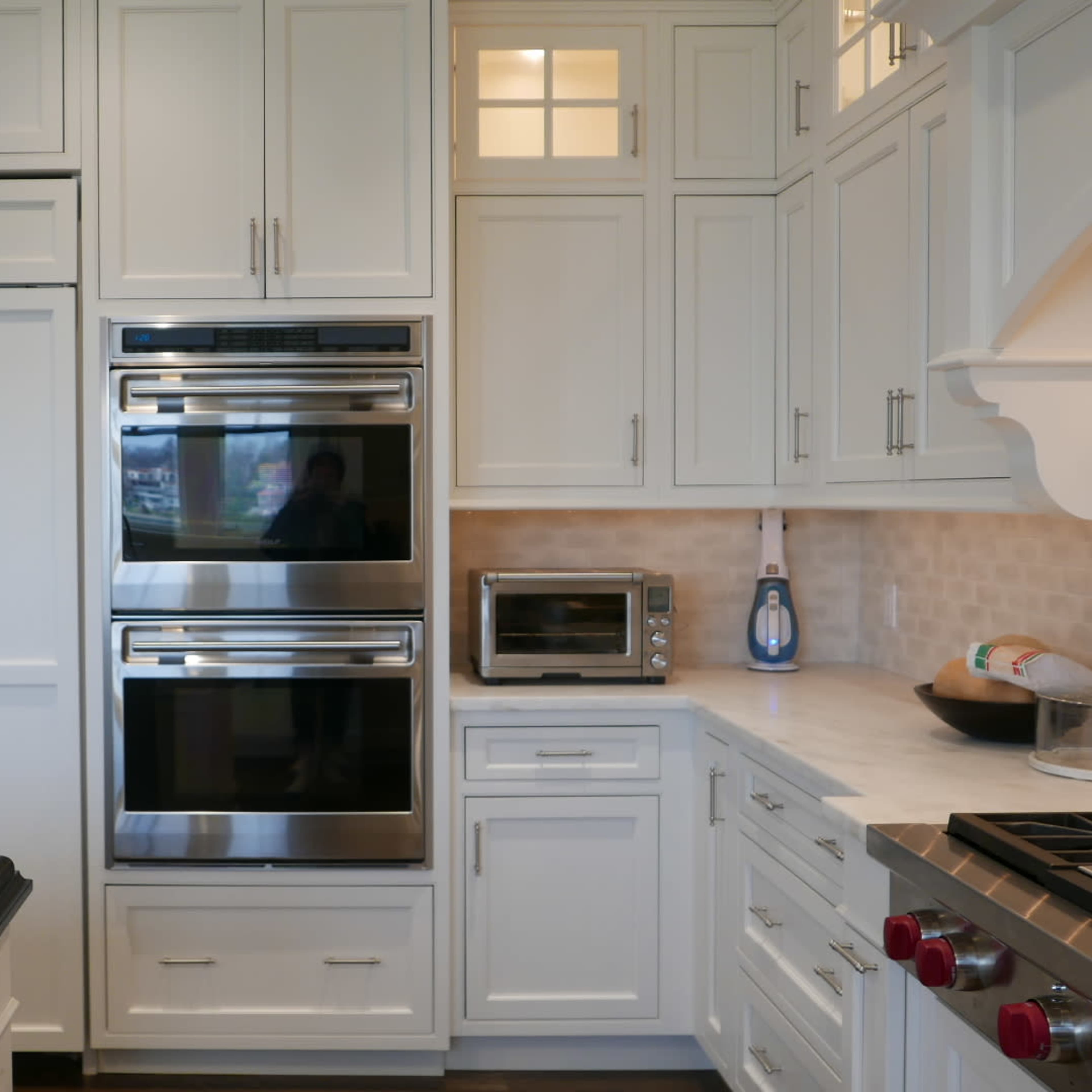 A modern kitchen features stainless steel appliances, including double ovens and a microwave, with white cabinetry and a dark countertop.