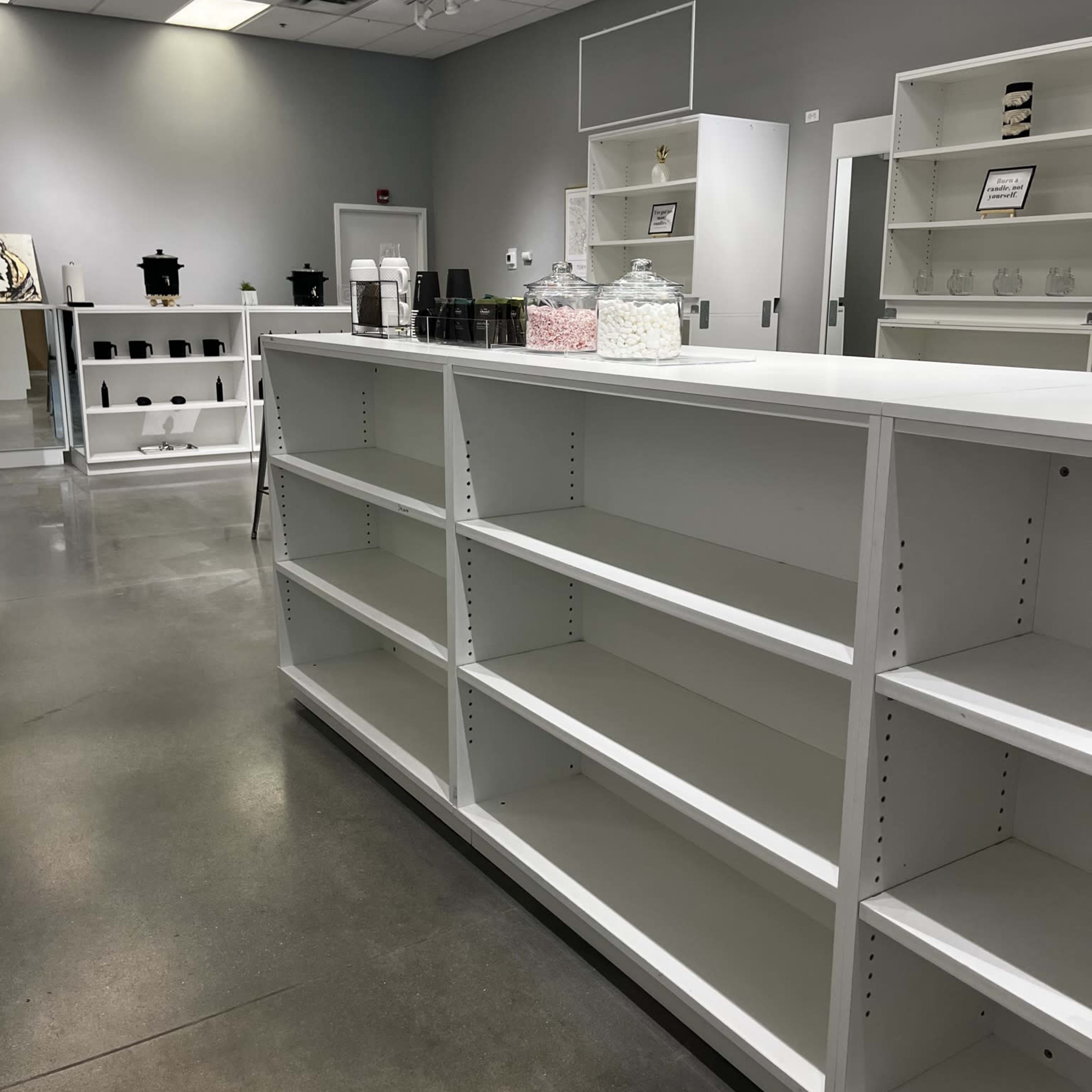 A spacious, vacant retail space with white shelving units and minimal decor.
