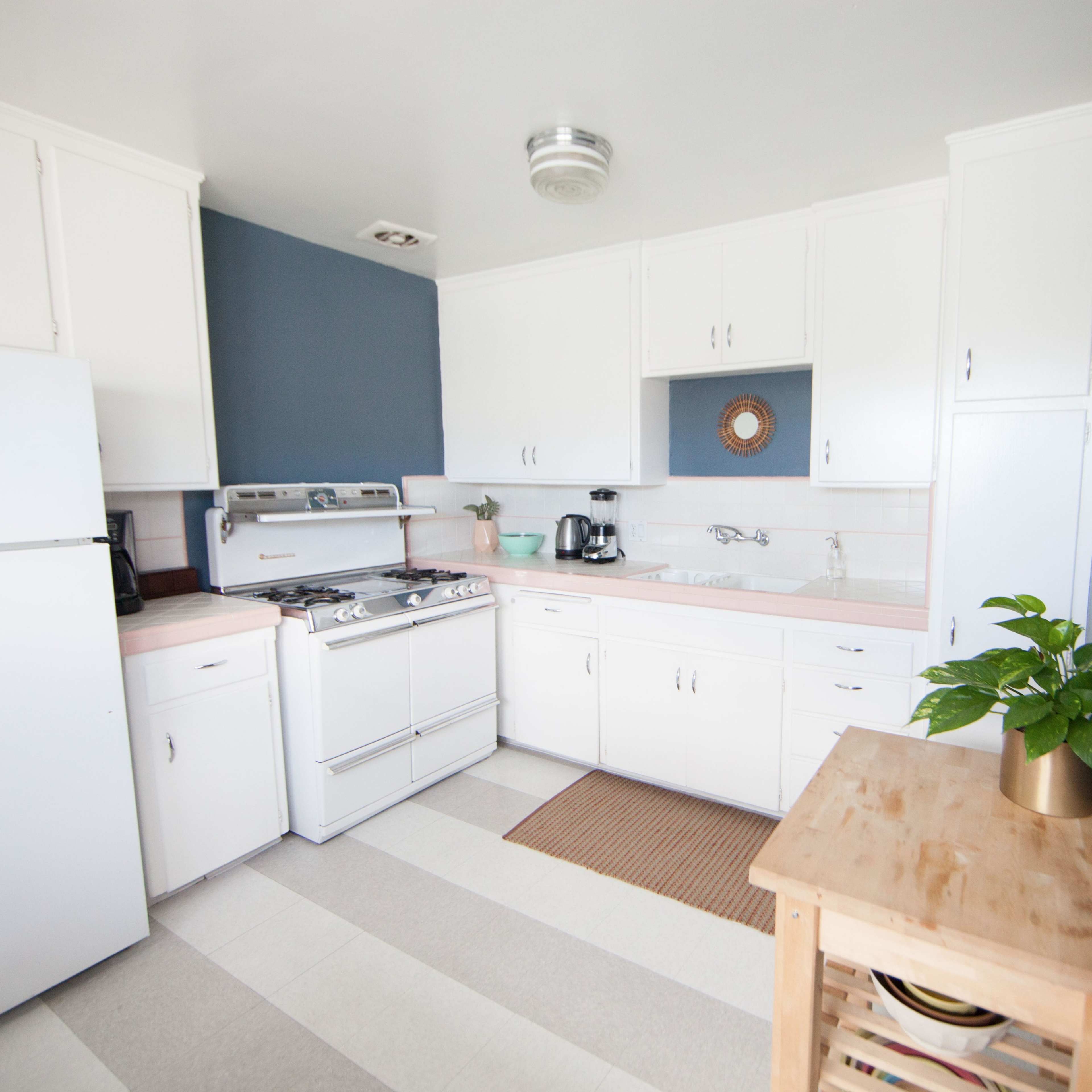 The kitchen features white cabinetry, a gray accent wall, a stove, and a small wooden table with a potted plant.