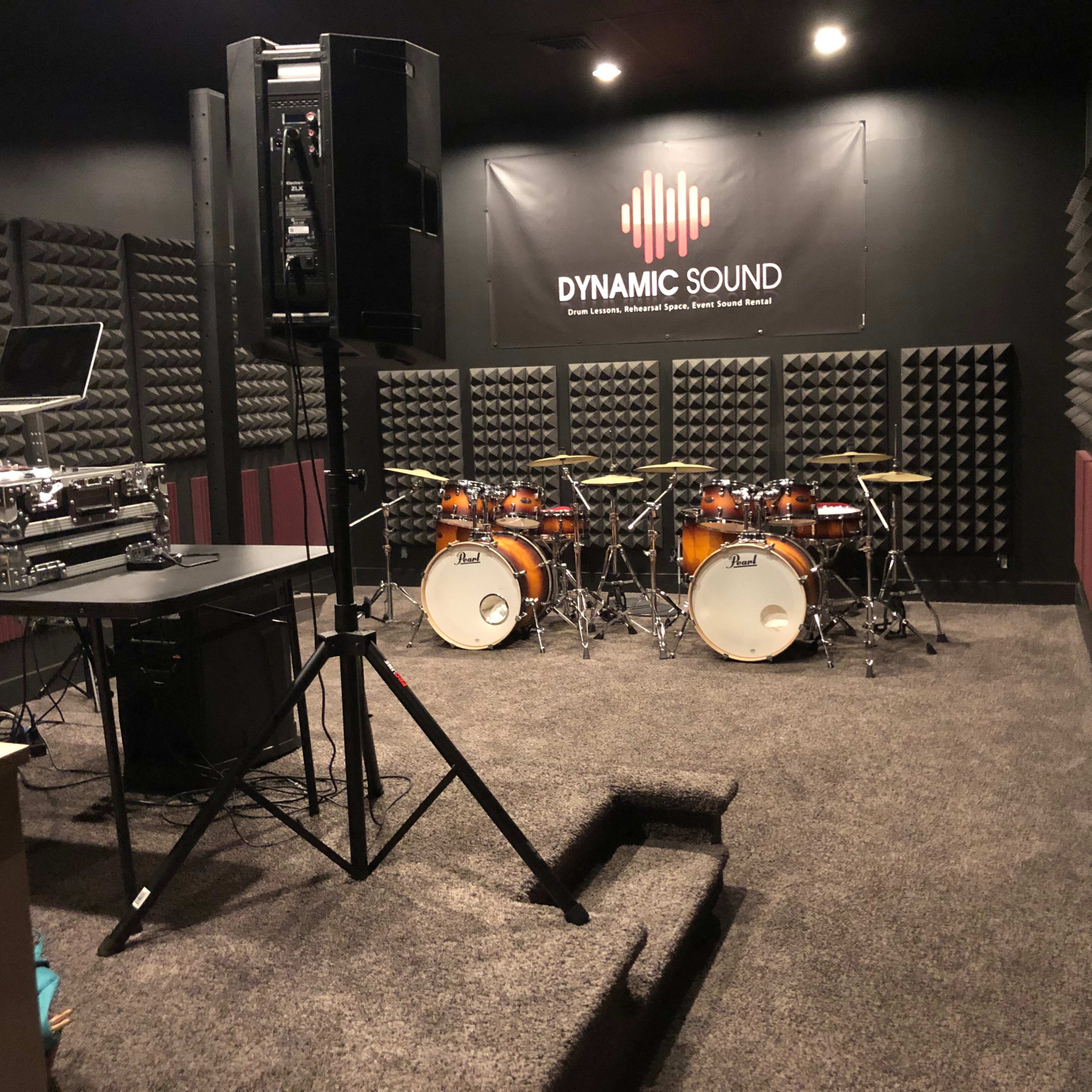 A soundproof rehearsal studio with a drum set, DJ equipment, and acoustic foam panels on the walls.