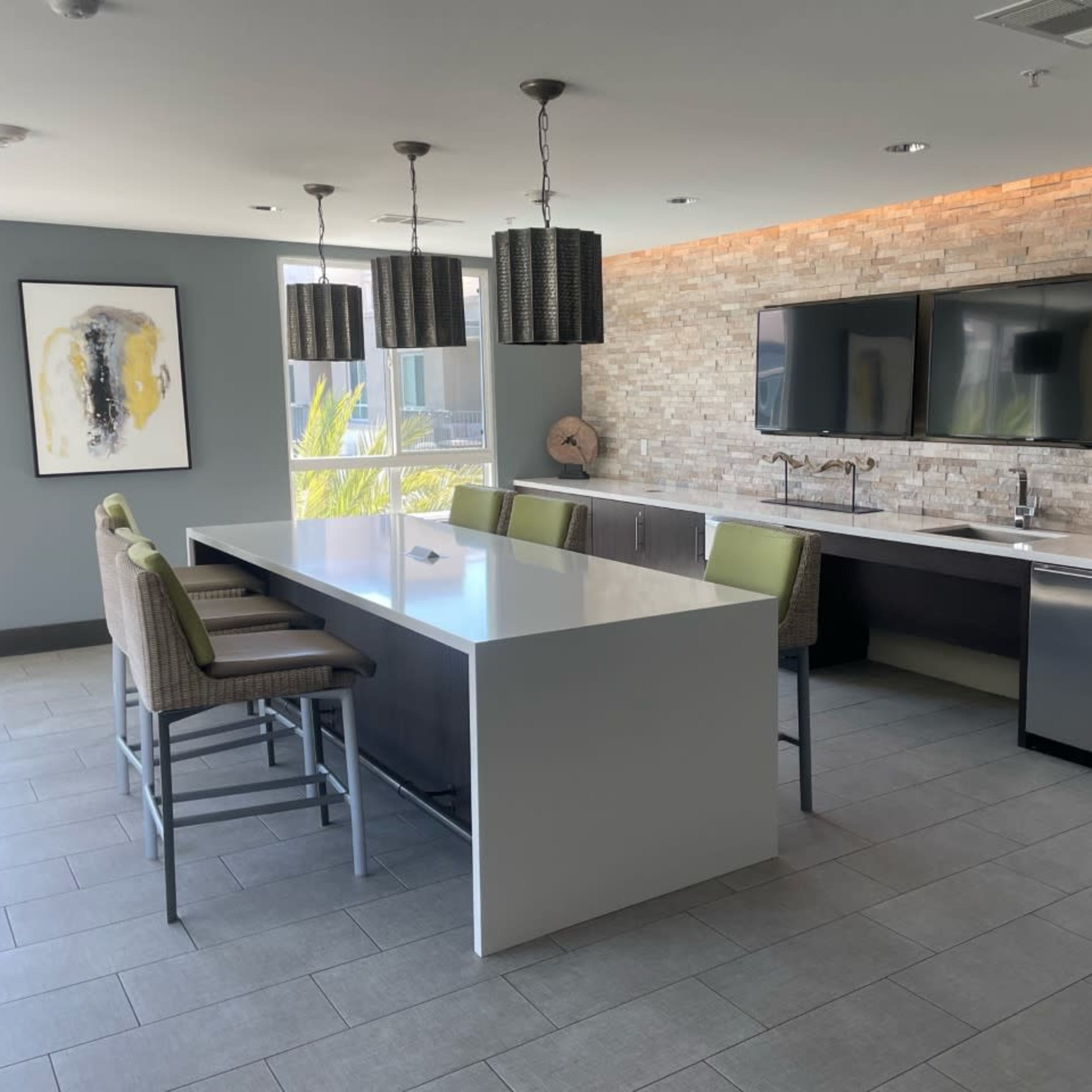 A modern kitchen features a large white island with bar seating, stainless steel appliances, and a stone accent wall.