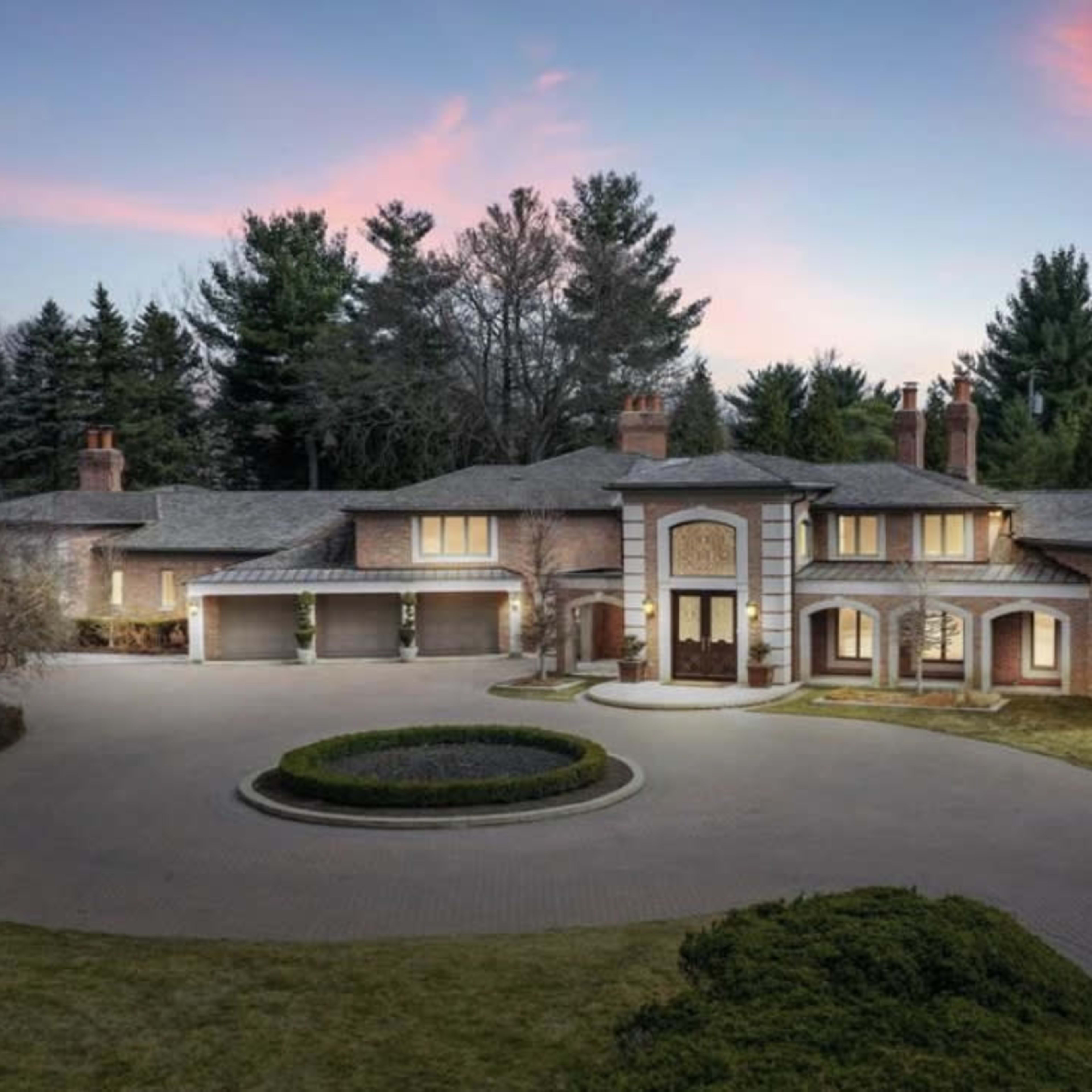 A large, modern brick house with numerous windows surrounded by well-maintained landscaping and a circular driveway.