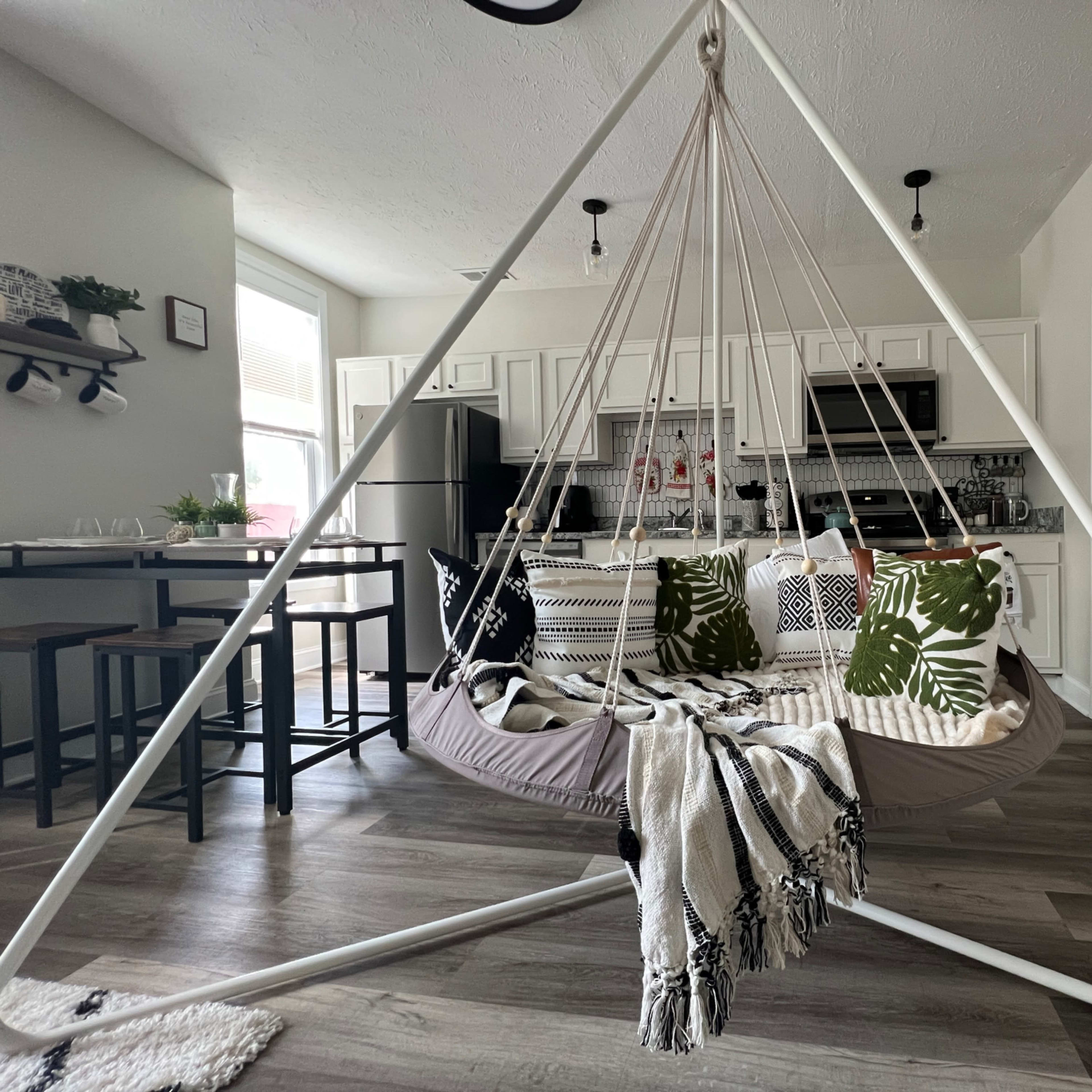 A triangular hanging chair with patterned cushions in a light-filled kitchen and dining area.