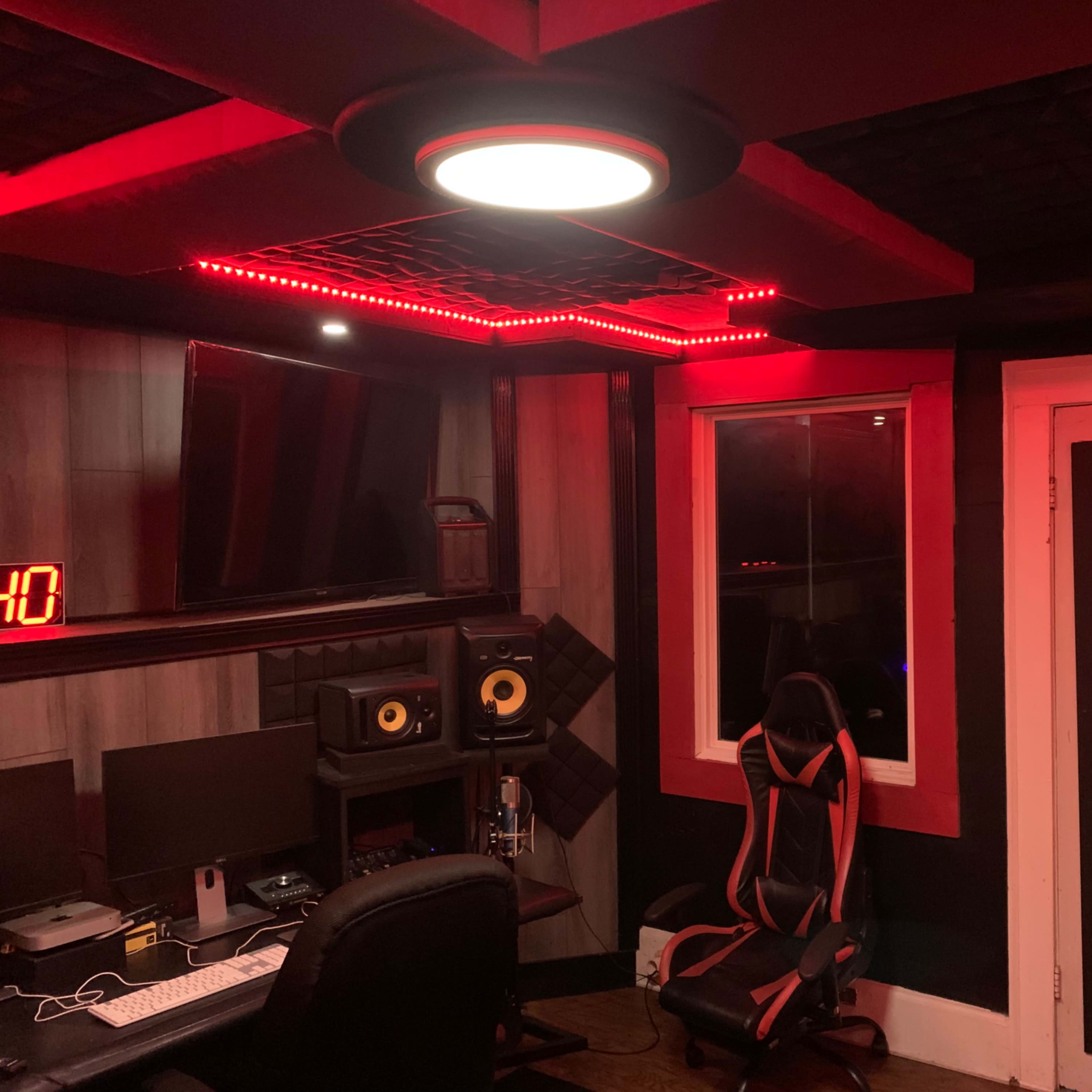 A music recording studio with red LED lighting, a computer desk, speakers, and a gaming chair.