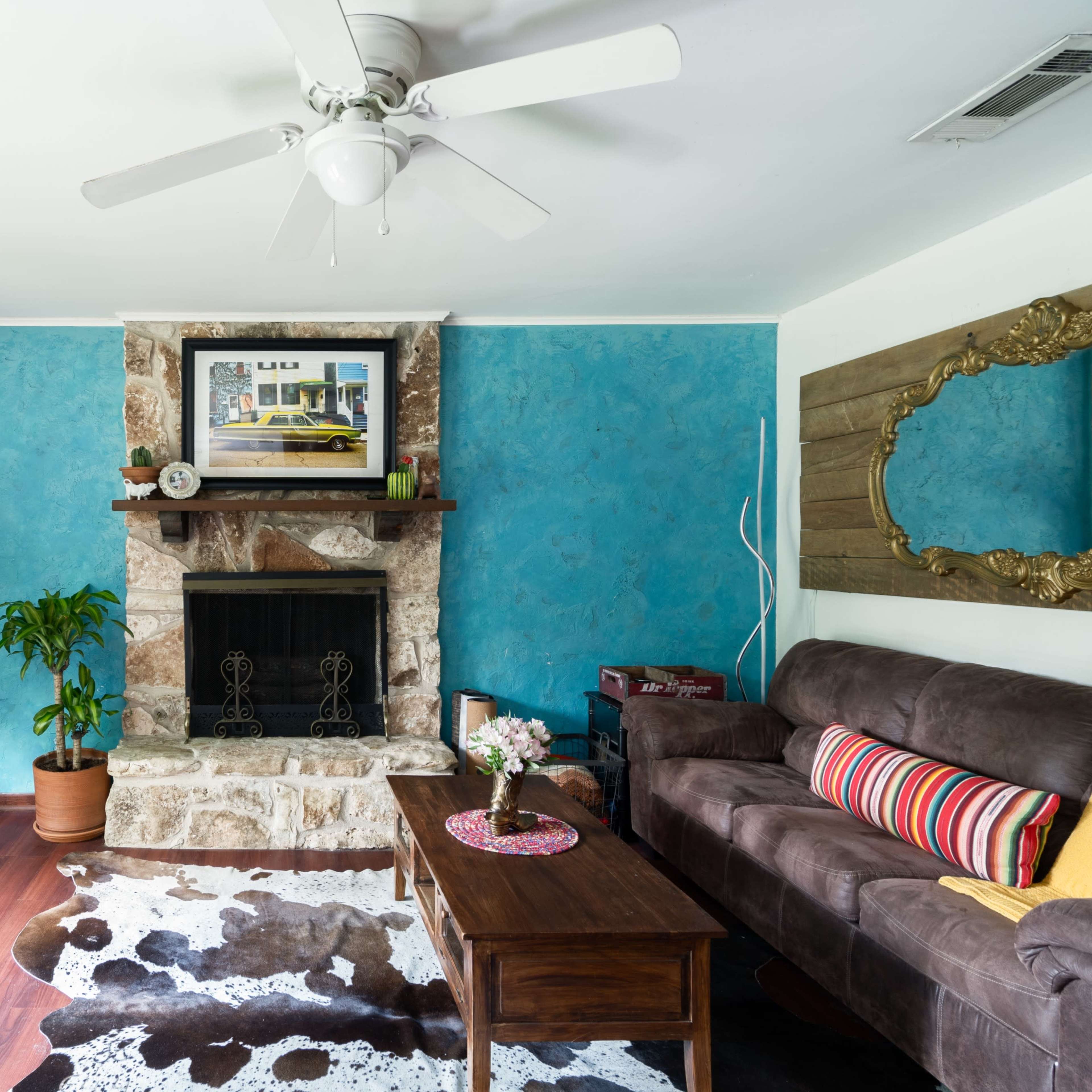 The living room features a stone fireplace with a colorful painting above it, a brown couch, a wooden coffee table, and blue walls.