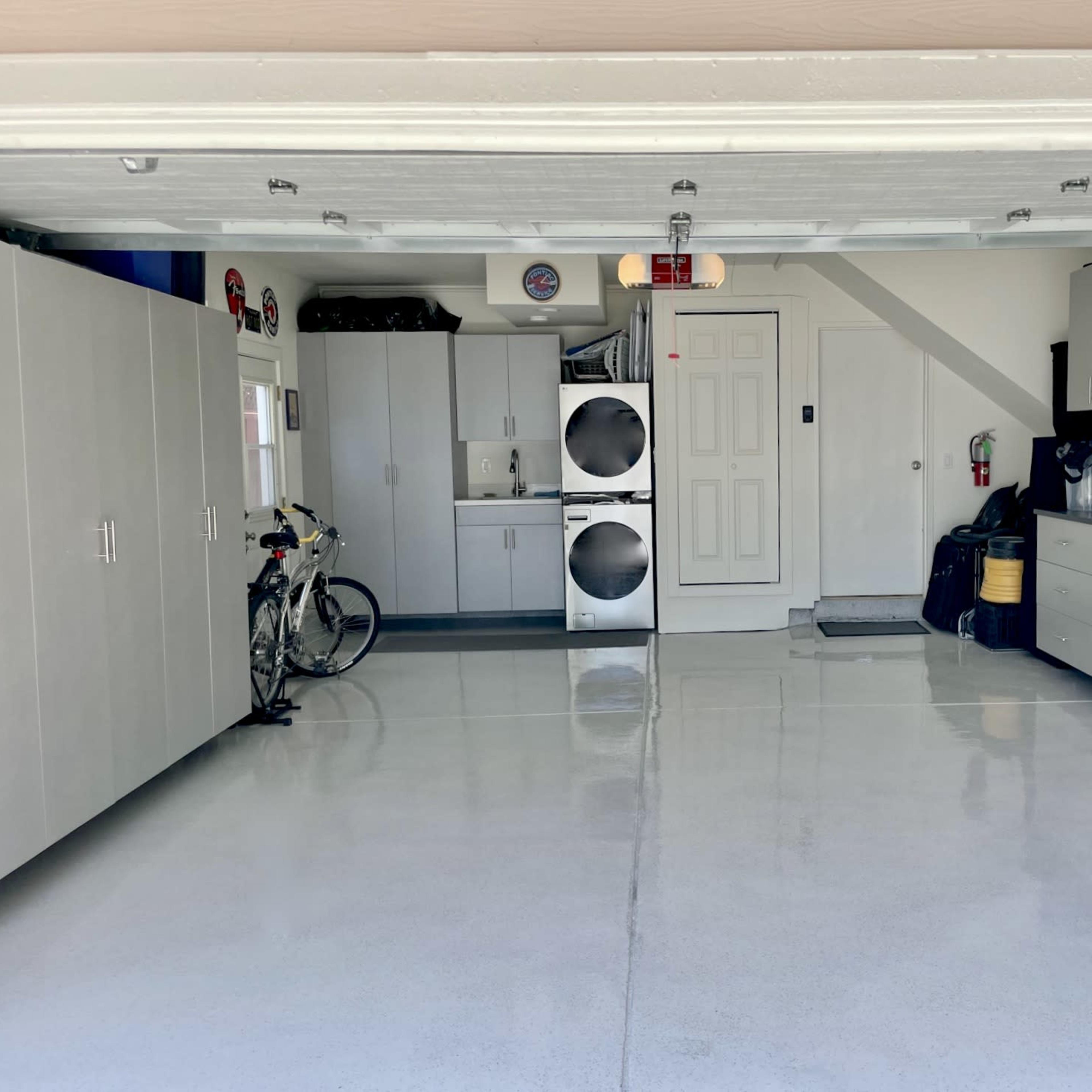 The garage features grey cabinets, laundry machines, and organized tool storage along with a bicycle parked in the corner.