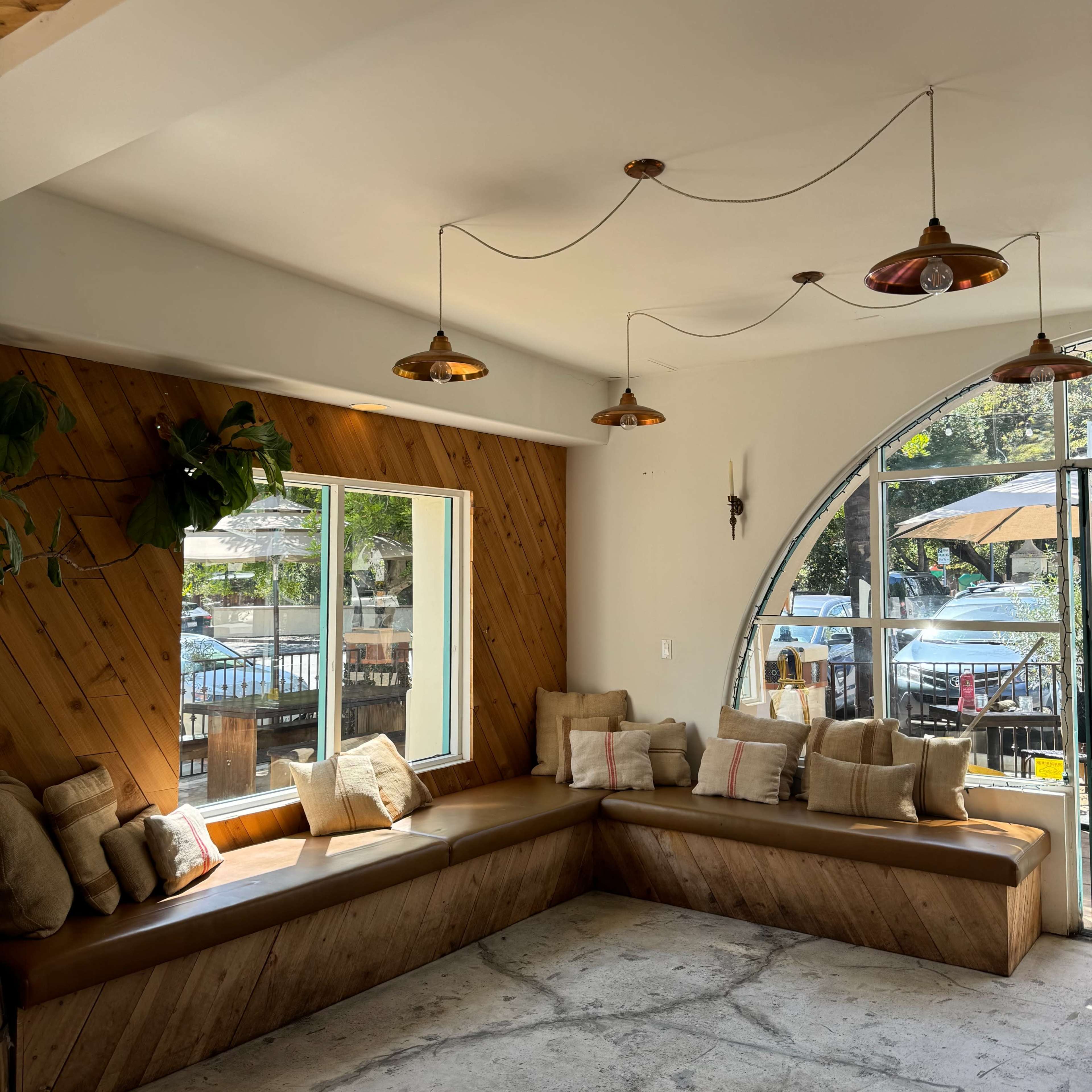 A modern, cozy seating area in a café with a curved window, wooden accents, and pendant lighting.