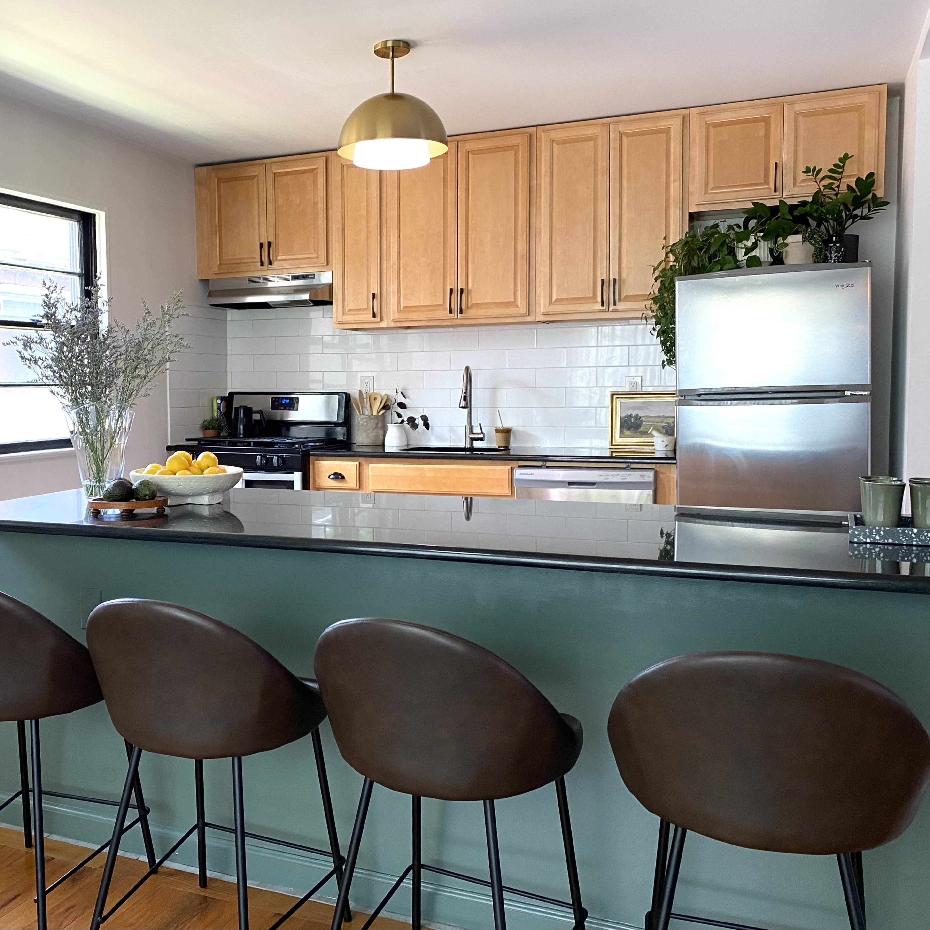 A modern kitchen features wooden cabinets, a stainless steel refrigerator, and four bar stools at a green kitchen island.