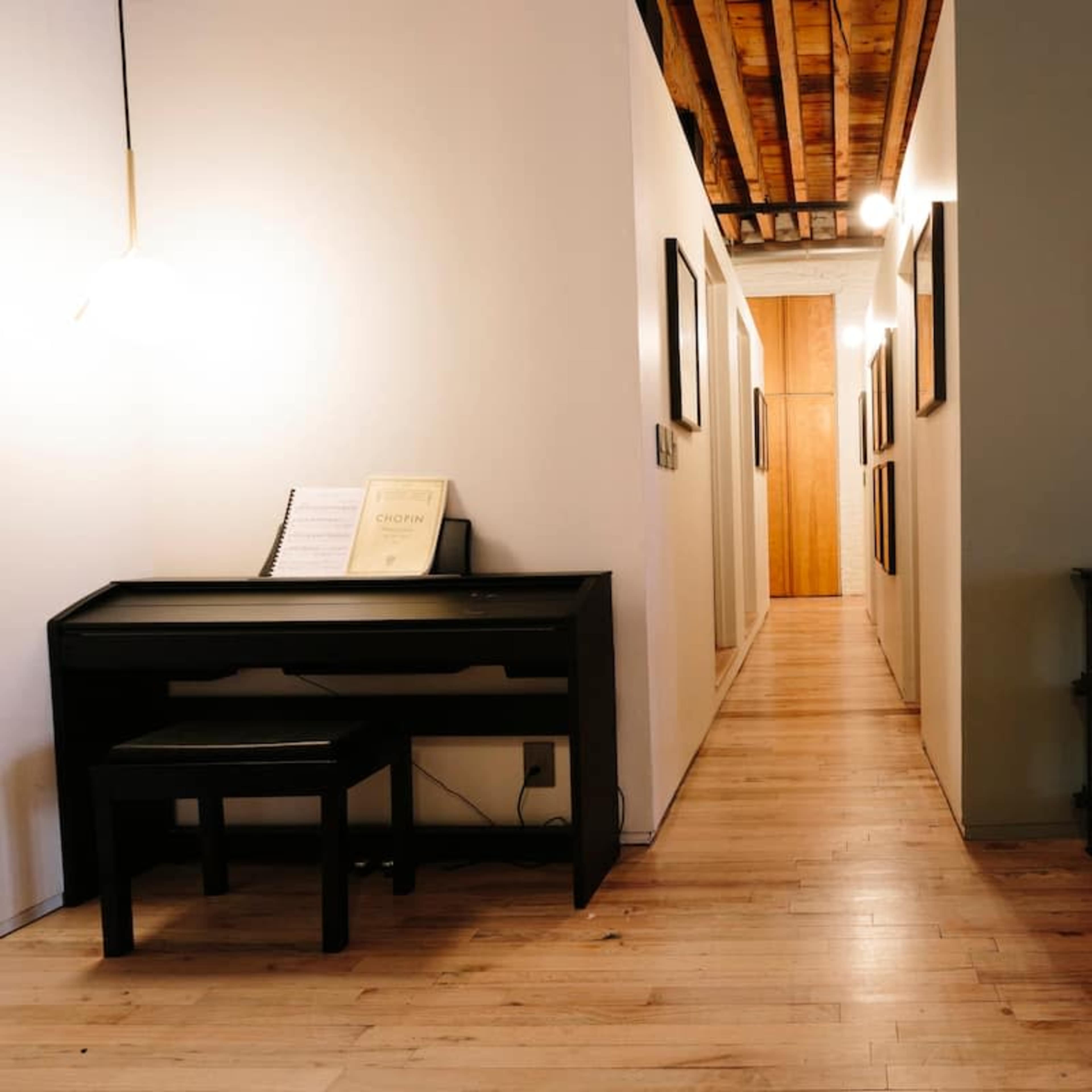 A narrow hallway features a black desk and chair on one side, with framed artwork lining the walls and a circular painting at the far end.