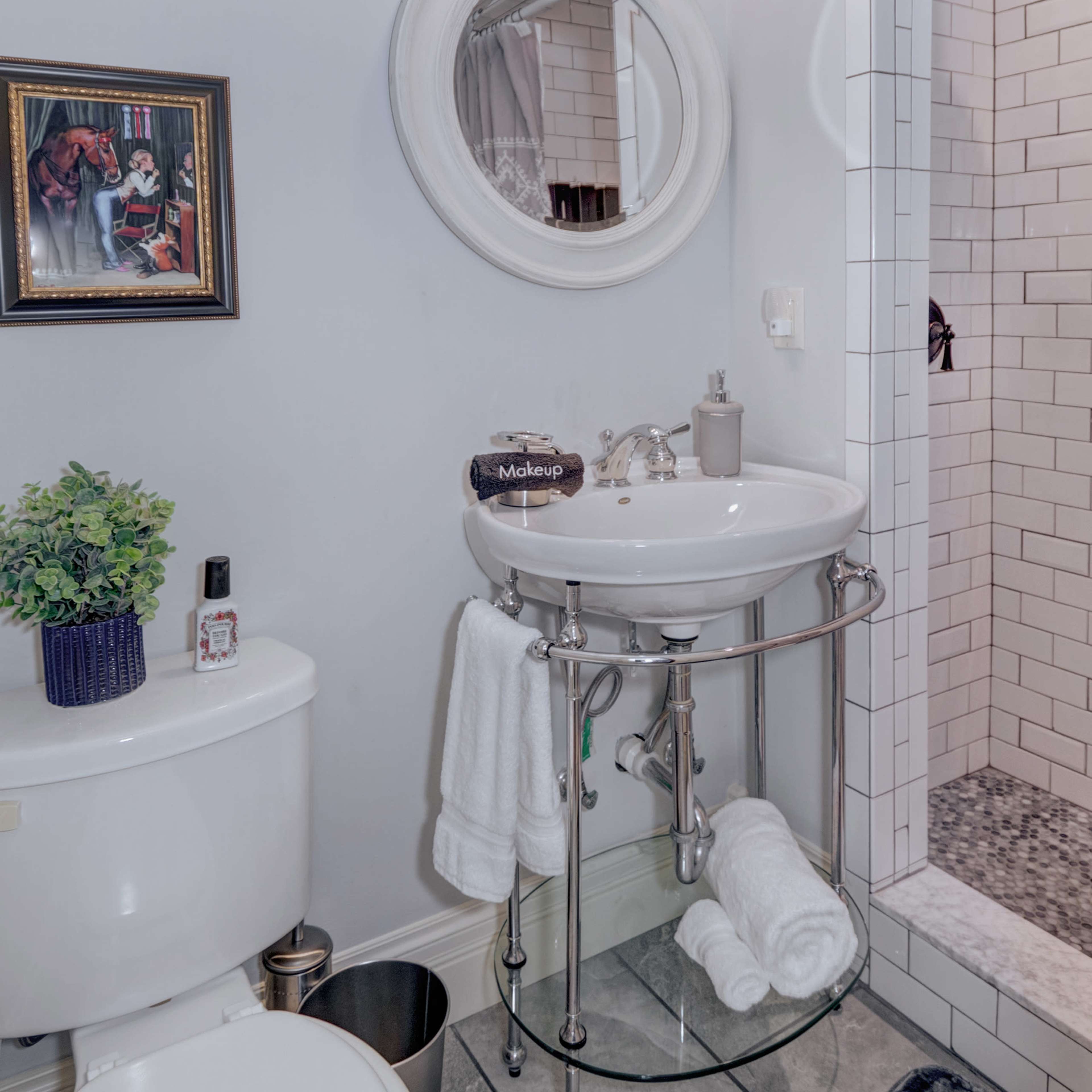 A compact bathroom featuring a round mirror above a pedestal sink, a toilet, and a glass shower enclosure with tile accents.