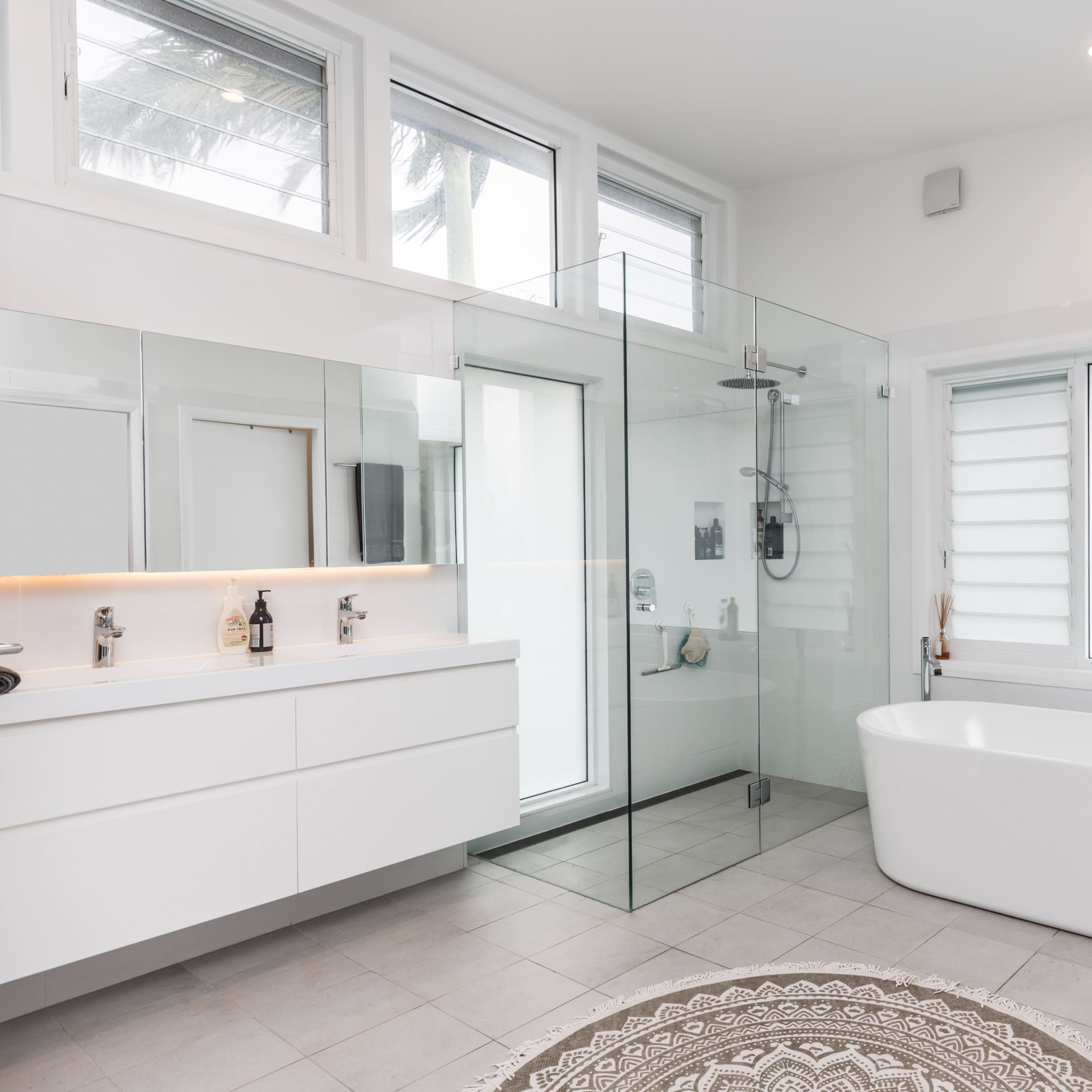 A modern bathroom featuring a glass shower enclosure, a freestanding bathtub, and dual sinks with a large mirror.