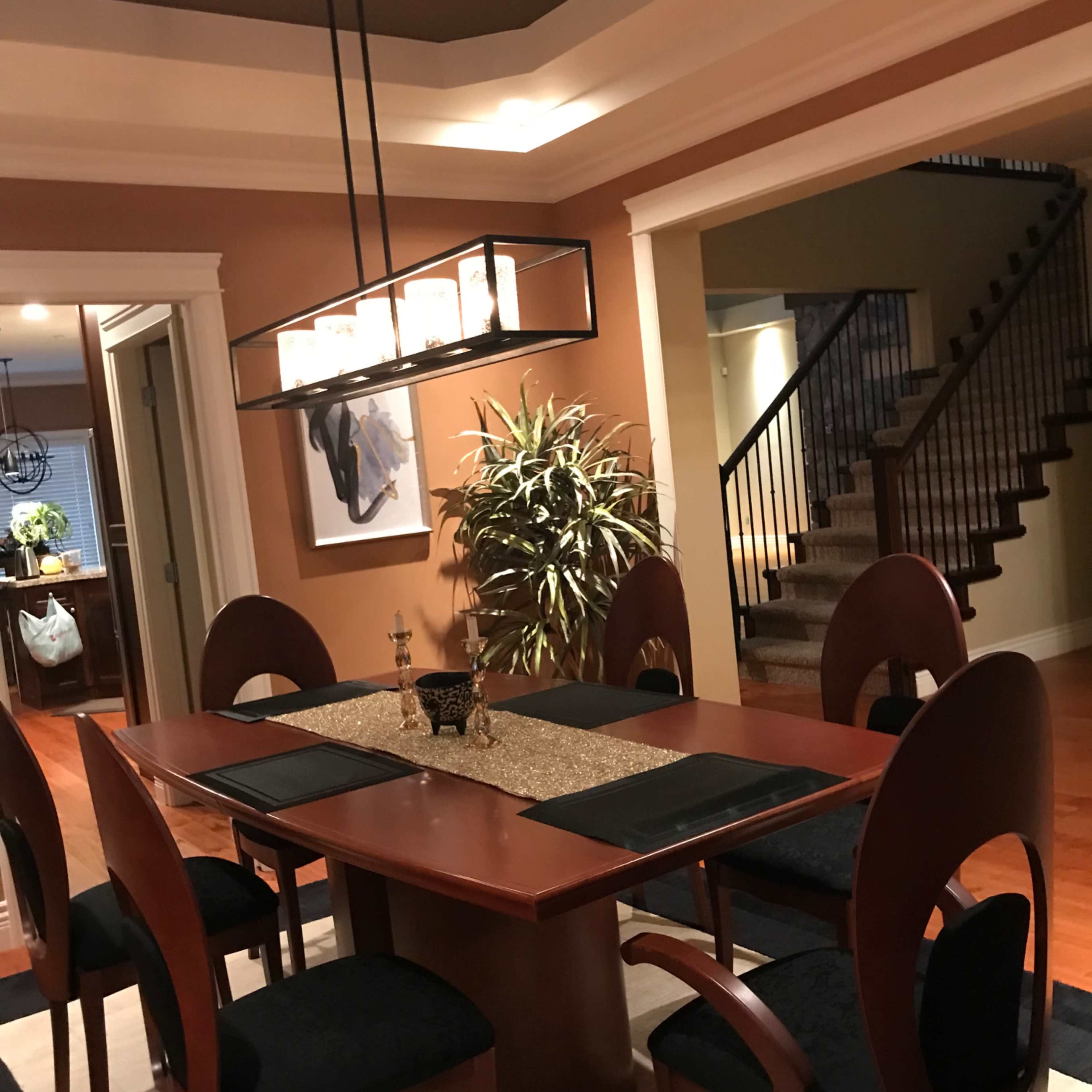A dining area with a rectangular wooden table surrounded by black chairs, a pendant light above, and a staircase leading to another level in the background.
