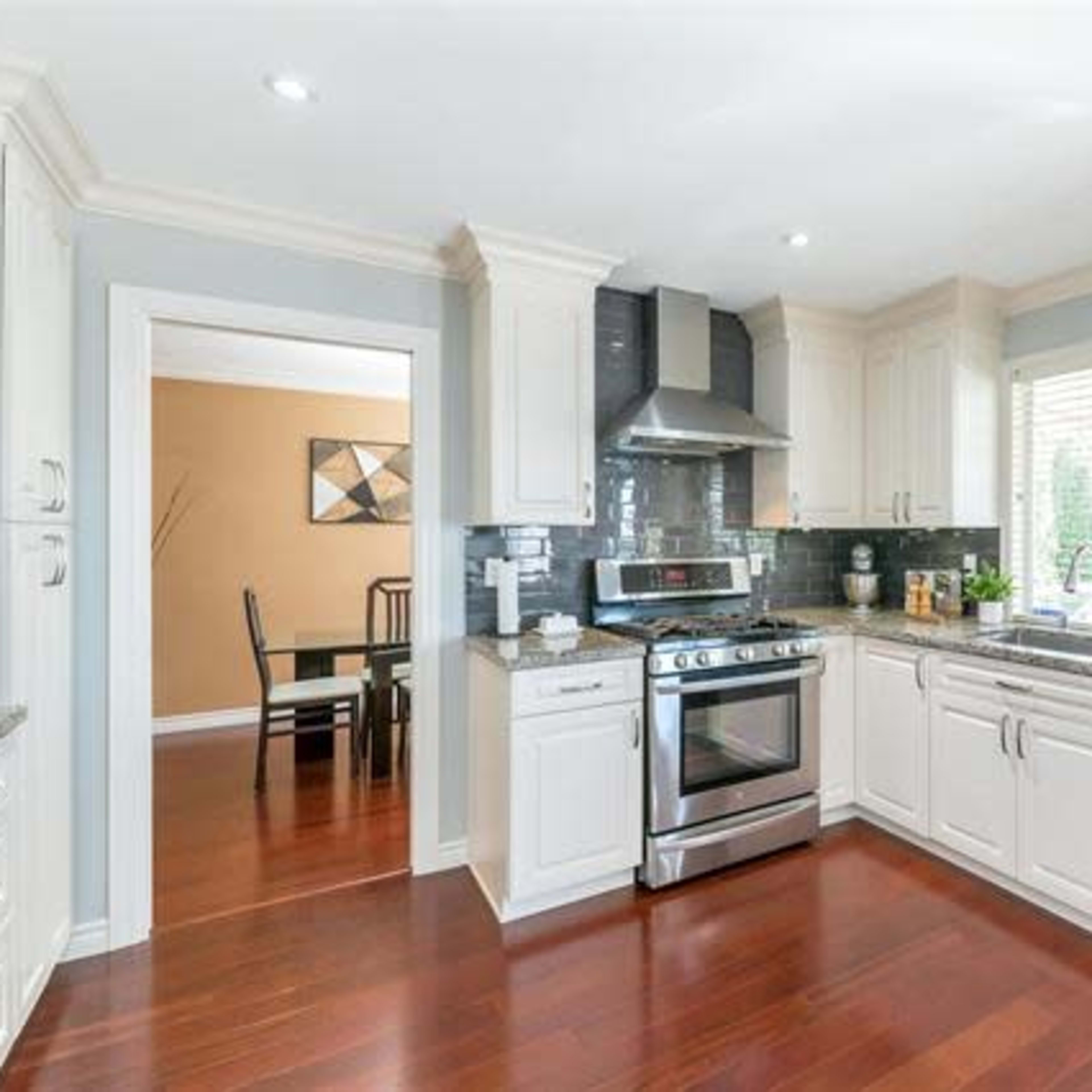 A modern kitchen with white cabinetry, a stainless steel stove and dishwasher, and a window overlooking a dining area.