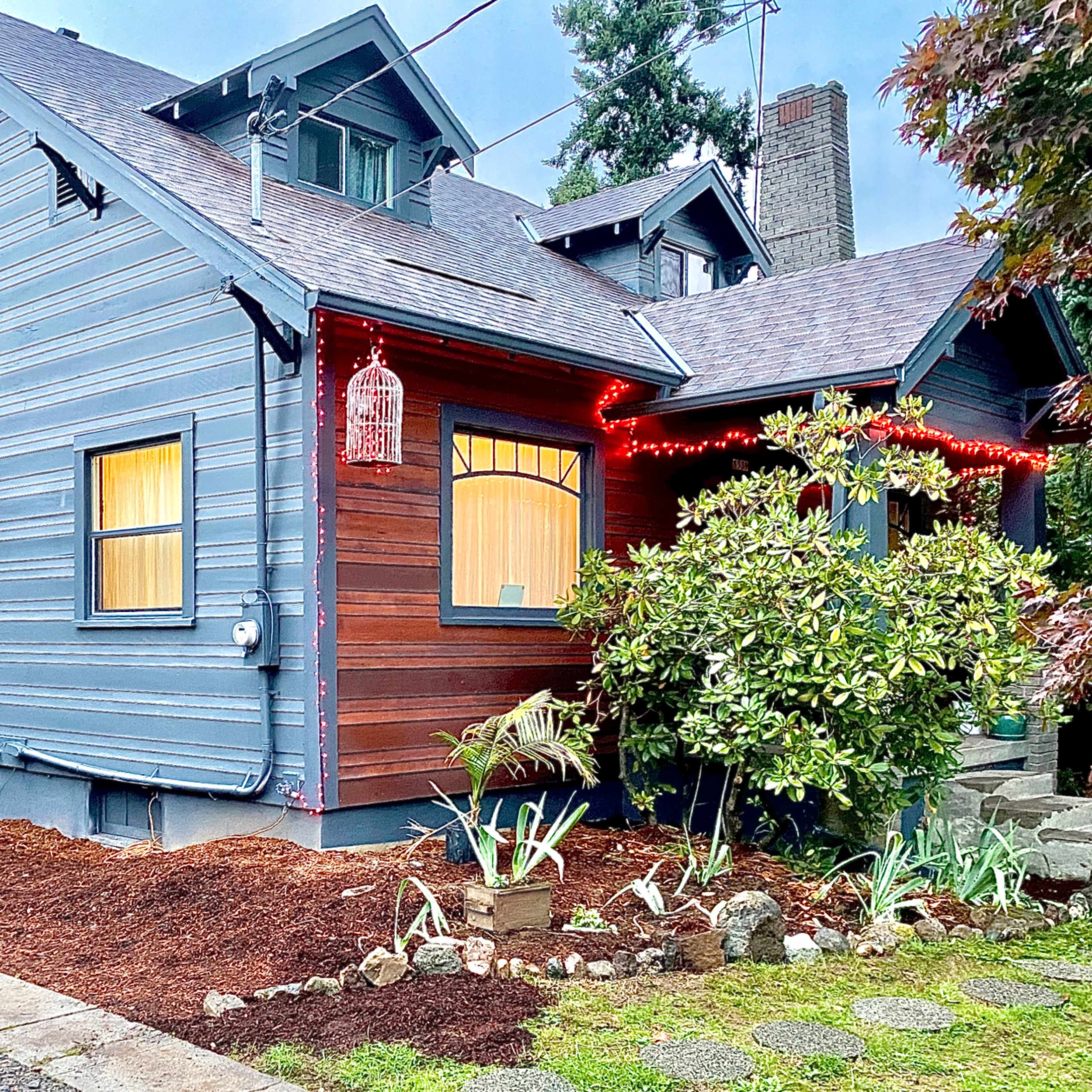A blue and brown two-story house with decorative lights and a landscaped front yard.