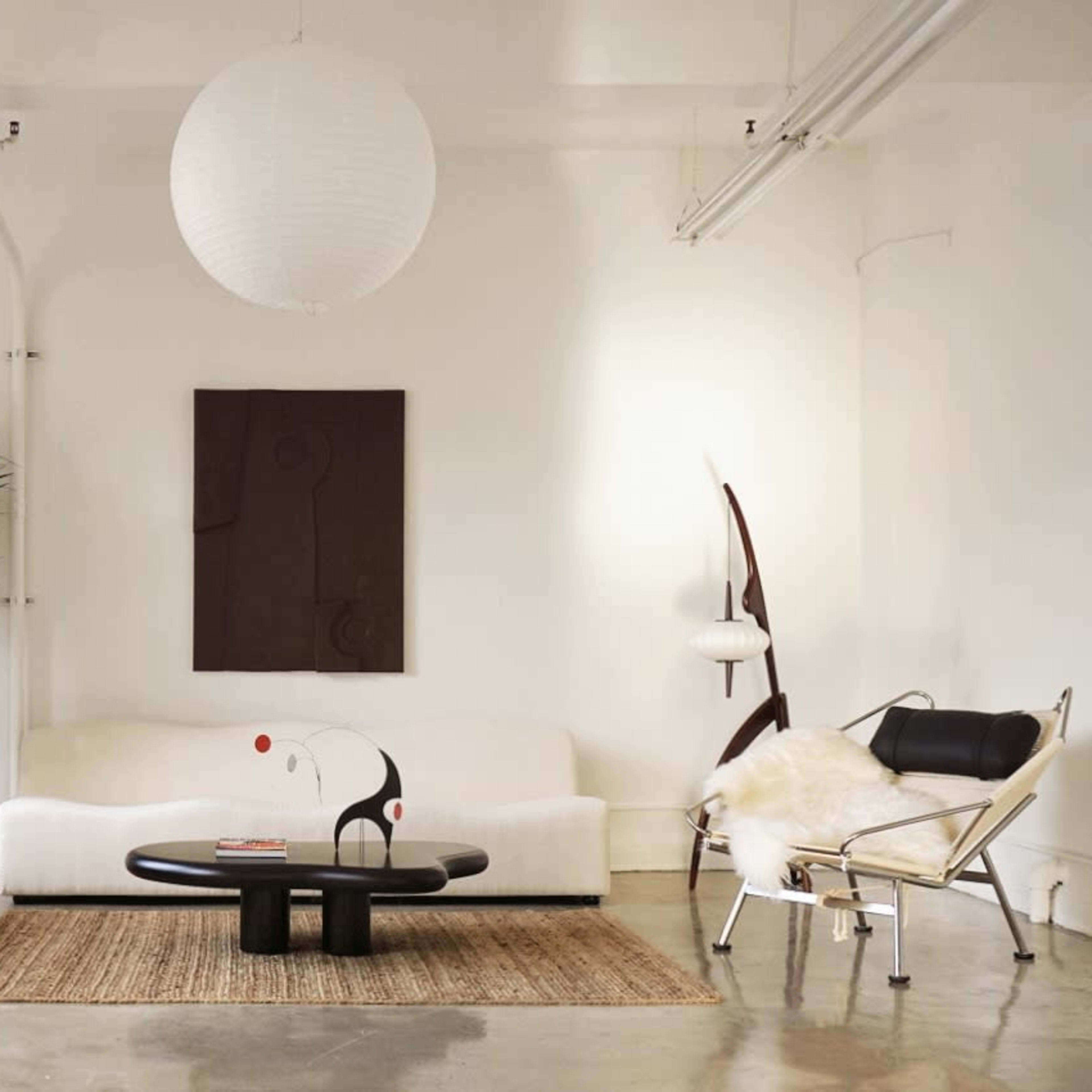 A bright living room features a white sofa, a round black coffee table, a textured rug, and a tall plant, complemented by modern art on the wall.