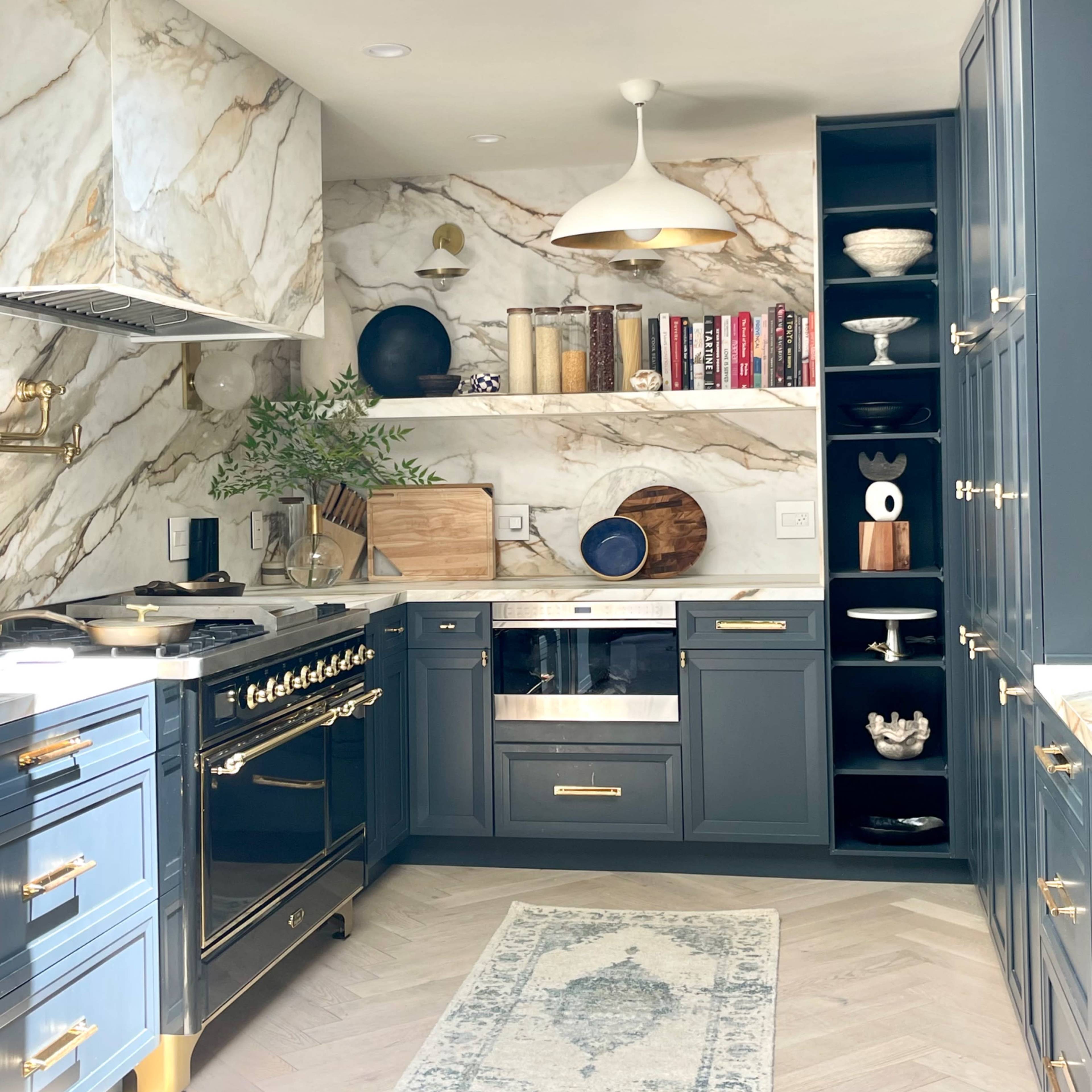 A modern kitchen featuring marble walls, dark blue cabinetry, a large stove, and open shelving with decorative items.