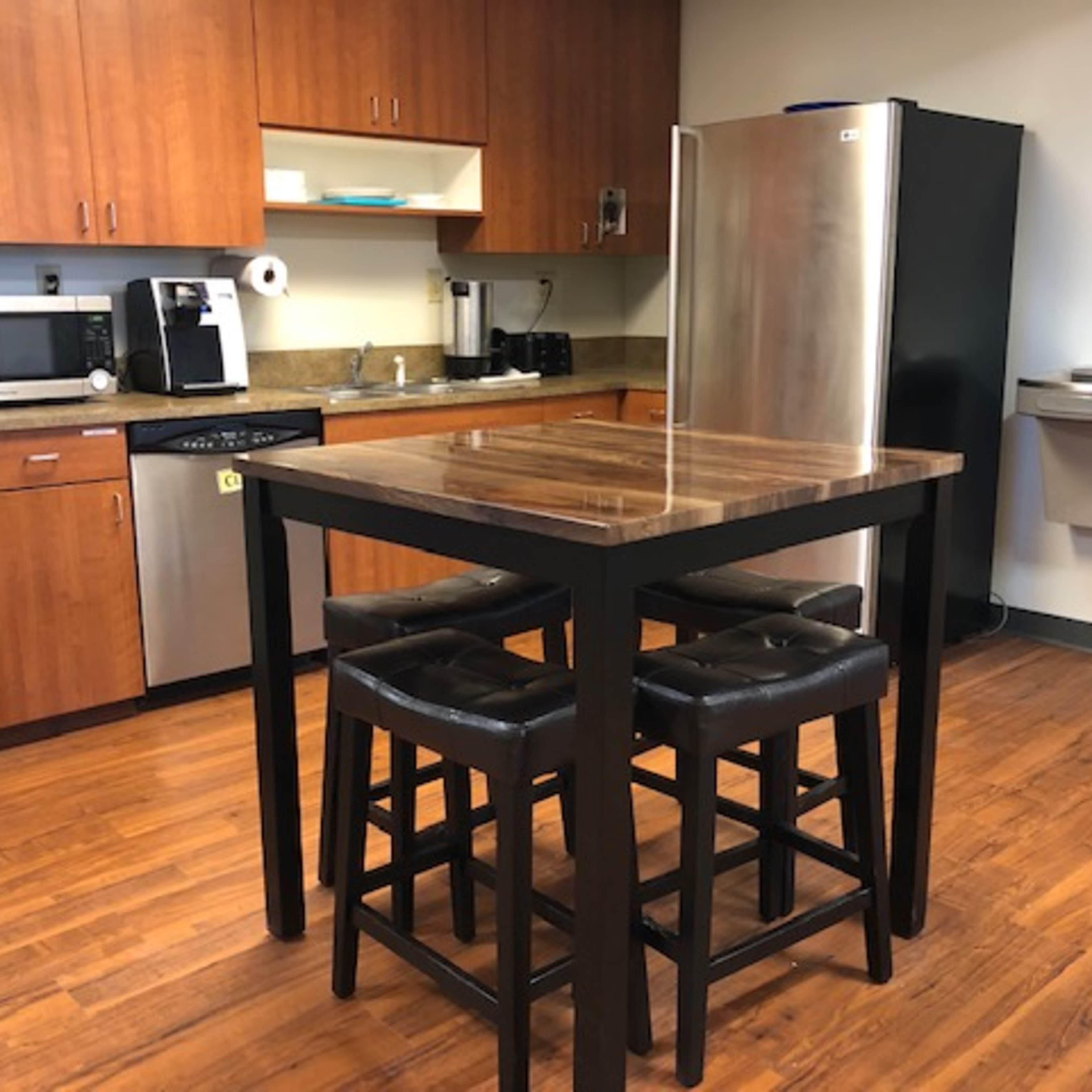 A kitchen area with wooden cabinets, stainless steel appliances, a tall table, and four black stools.