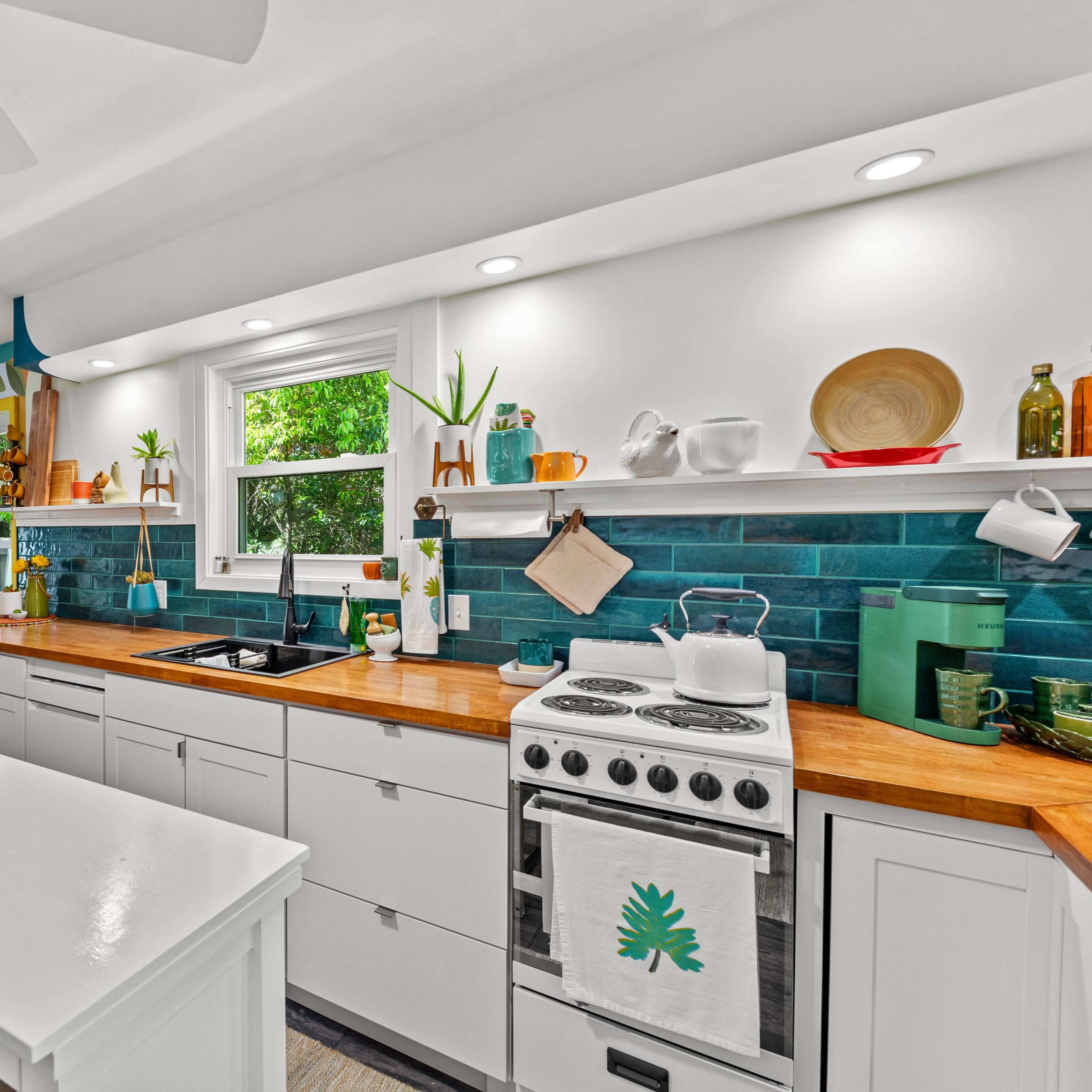 A bright kitchen features white cabinetry, a wooden countertop, a vintage stove, and shelves adorned with plants and decorative items.