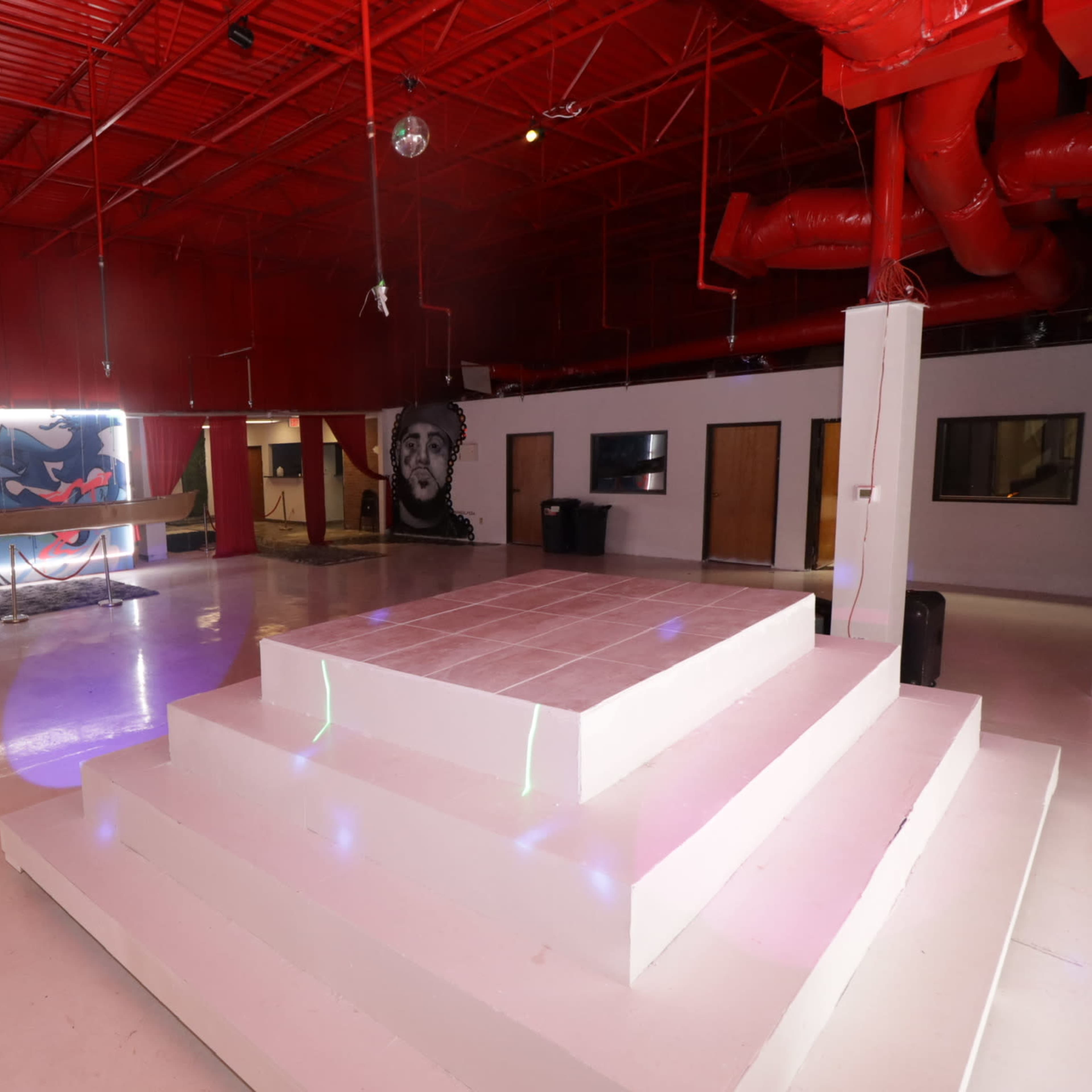 A spacious interior with a raised white platform, red walls, and a colorful mural on one side.