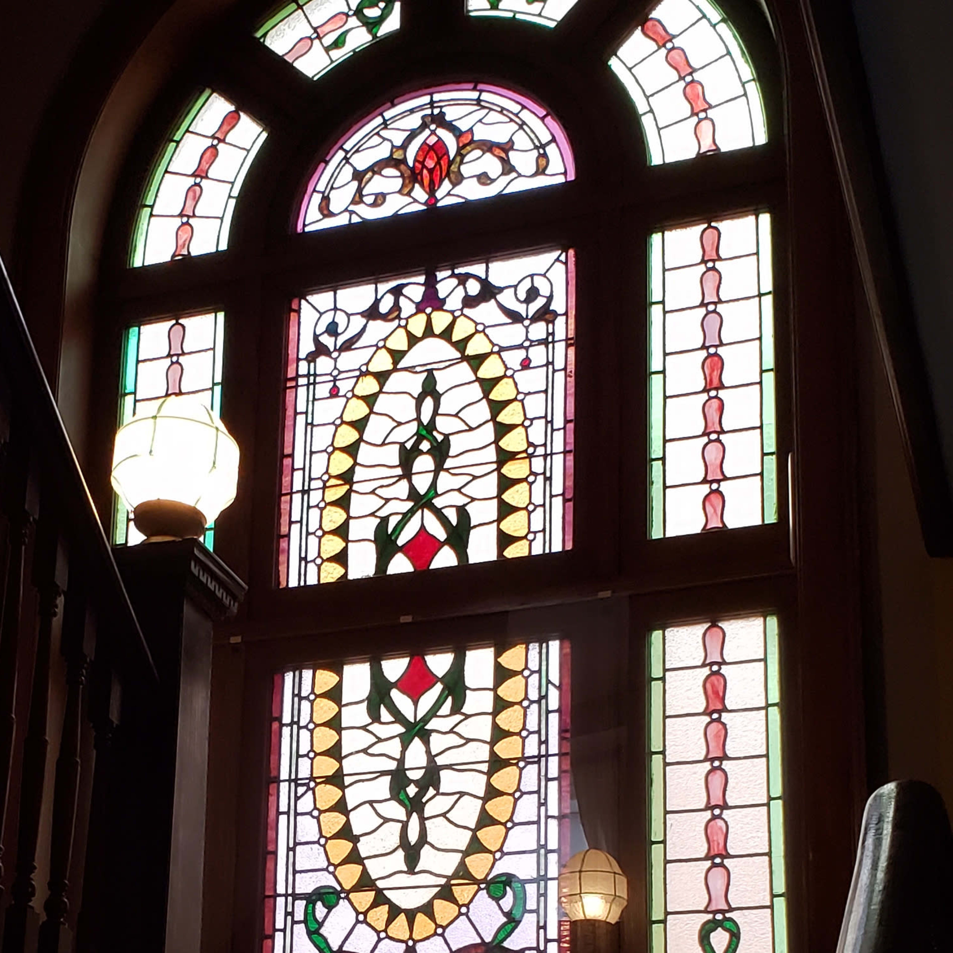 A staircase leading to an upper floor, with a large stained glass window featuring intricate patterns and colors.