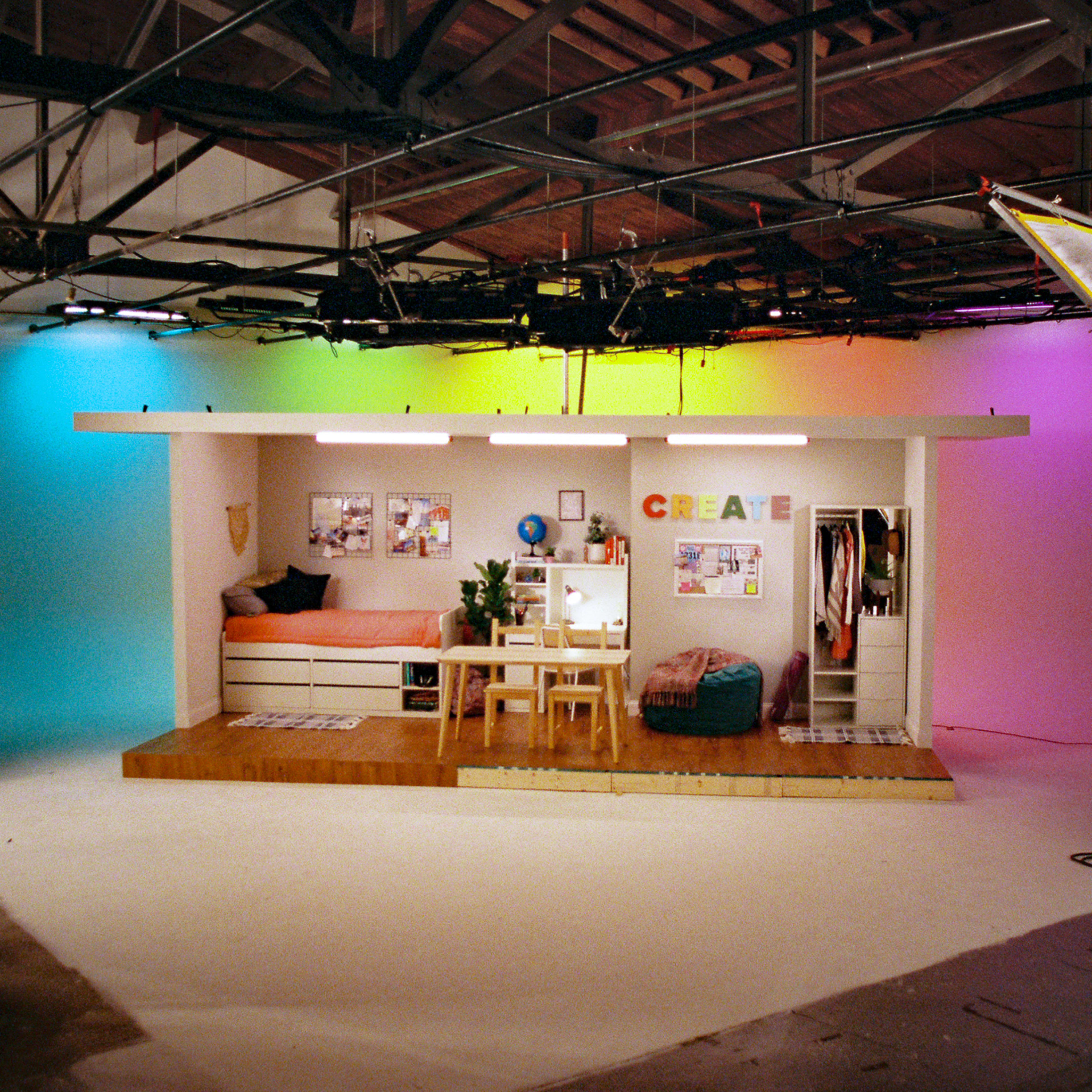 A creative studio setup with a small bedroom area and various decorations against colorful backdrop lighting.