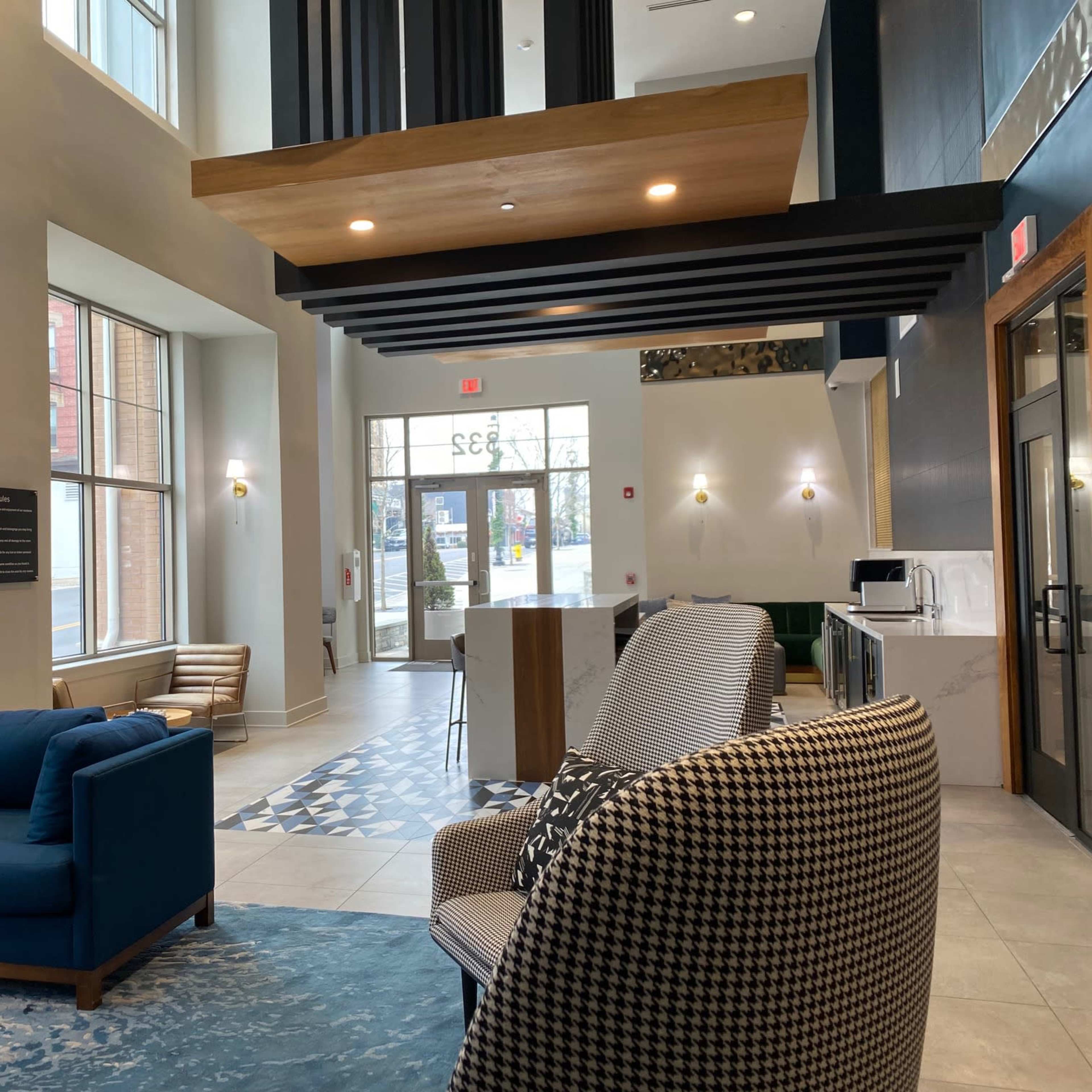 A modern lobby with a blue couch, patterned chairs, and large windows allowing natural light to enter the space.