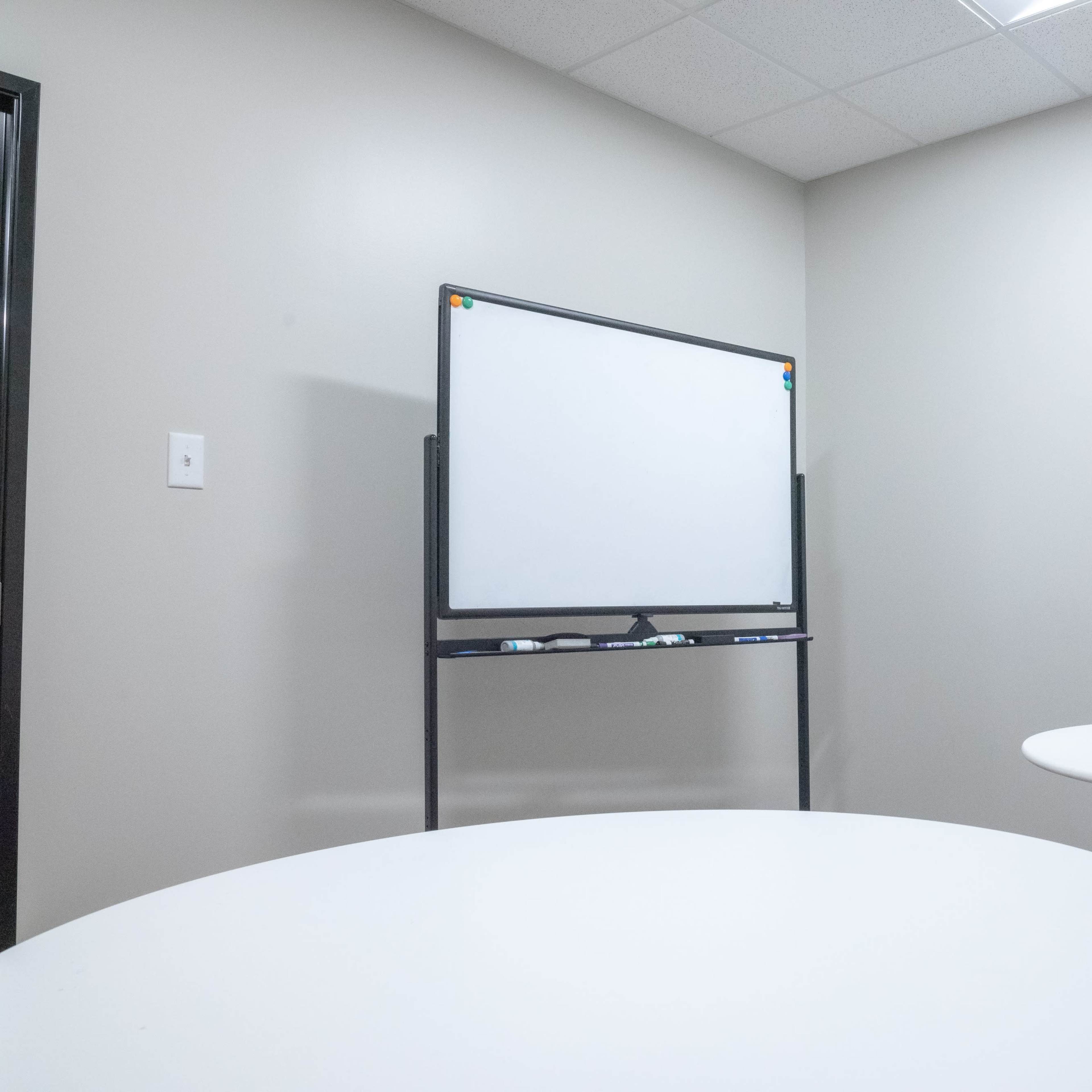 A small meeting room features two round tables and a whiteboard on a stand against a wall.