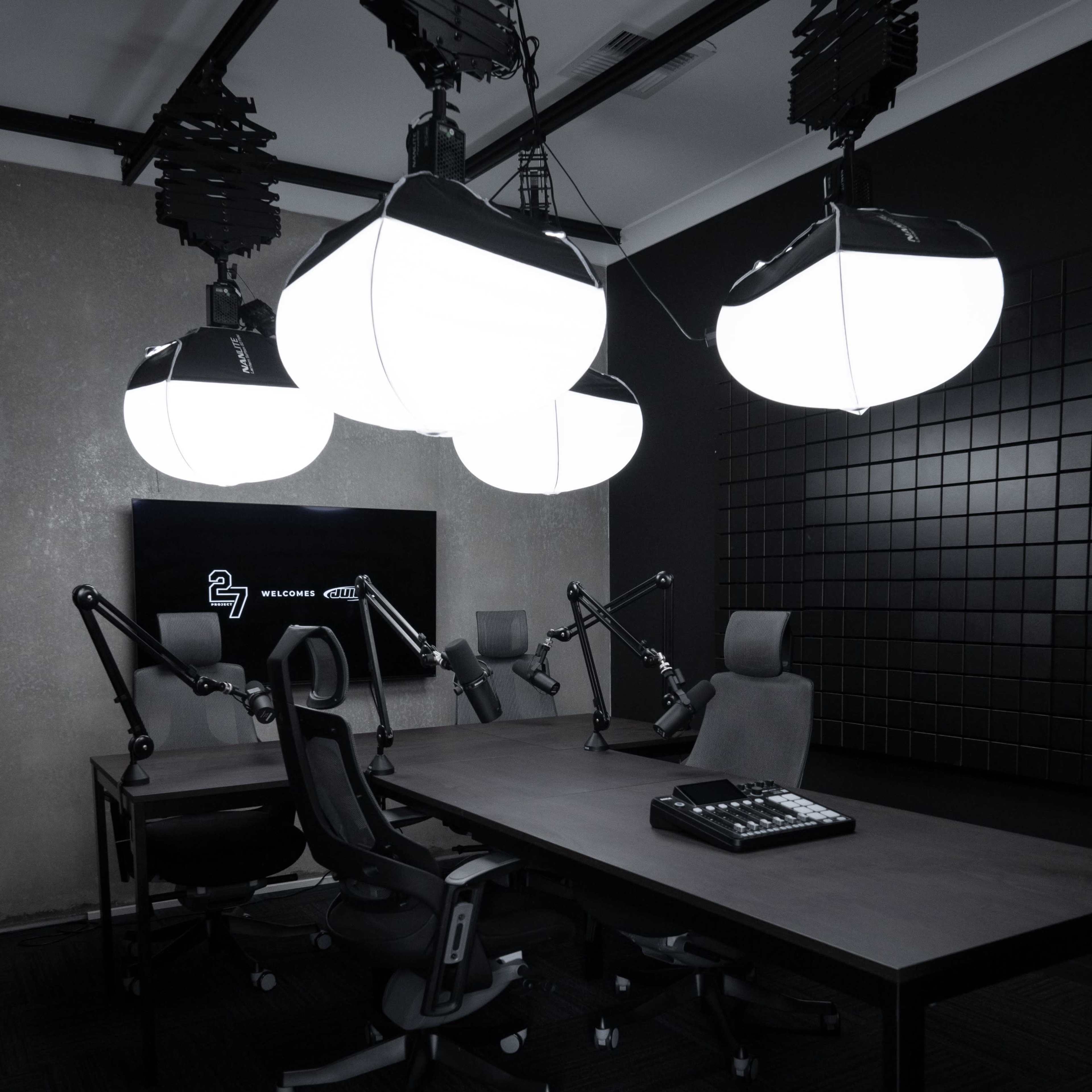 A modern recording studio equipped with a large table, adjustable chairs, and overhead lighting.