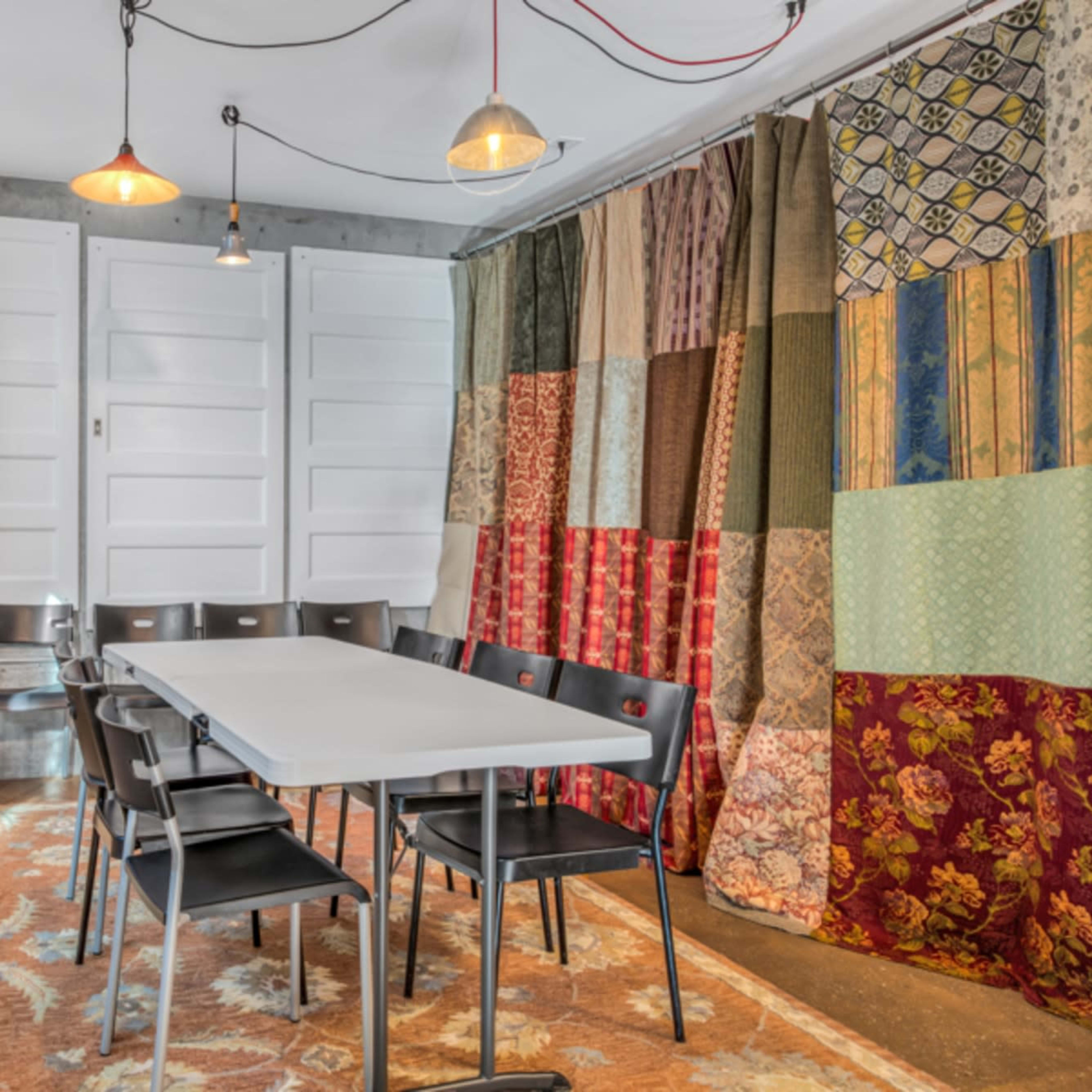 A small meeting room features a long table surrounded by black chairs, with colorful fabric drapes and a violin mounted on the wall.