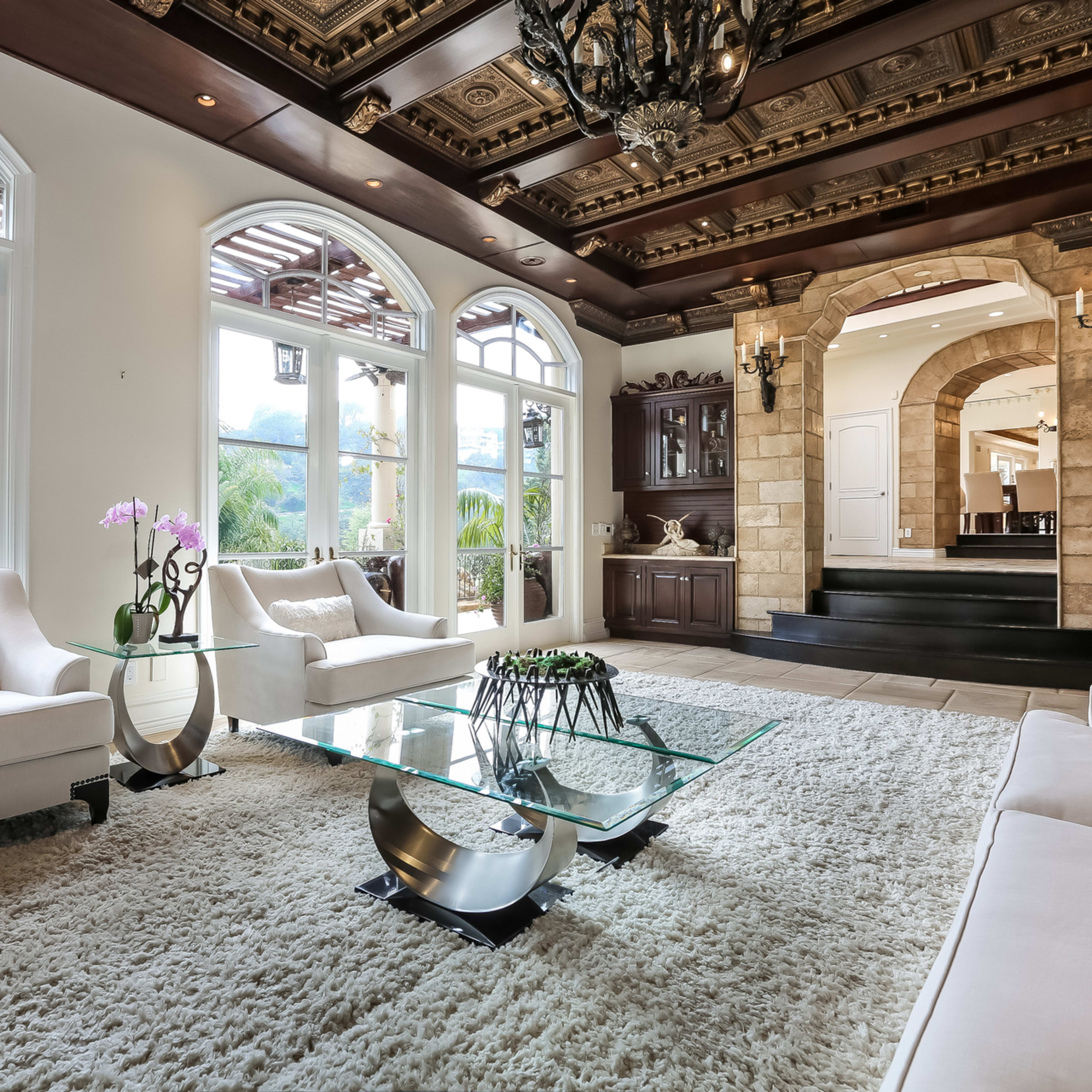 A spacious living room with elegant furnishings, a glass coffee table, and a decorative ceiling.