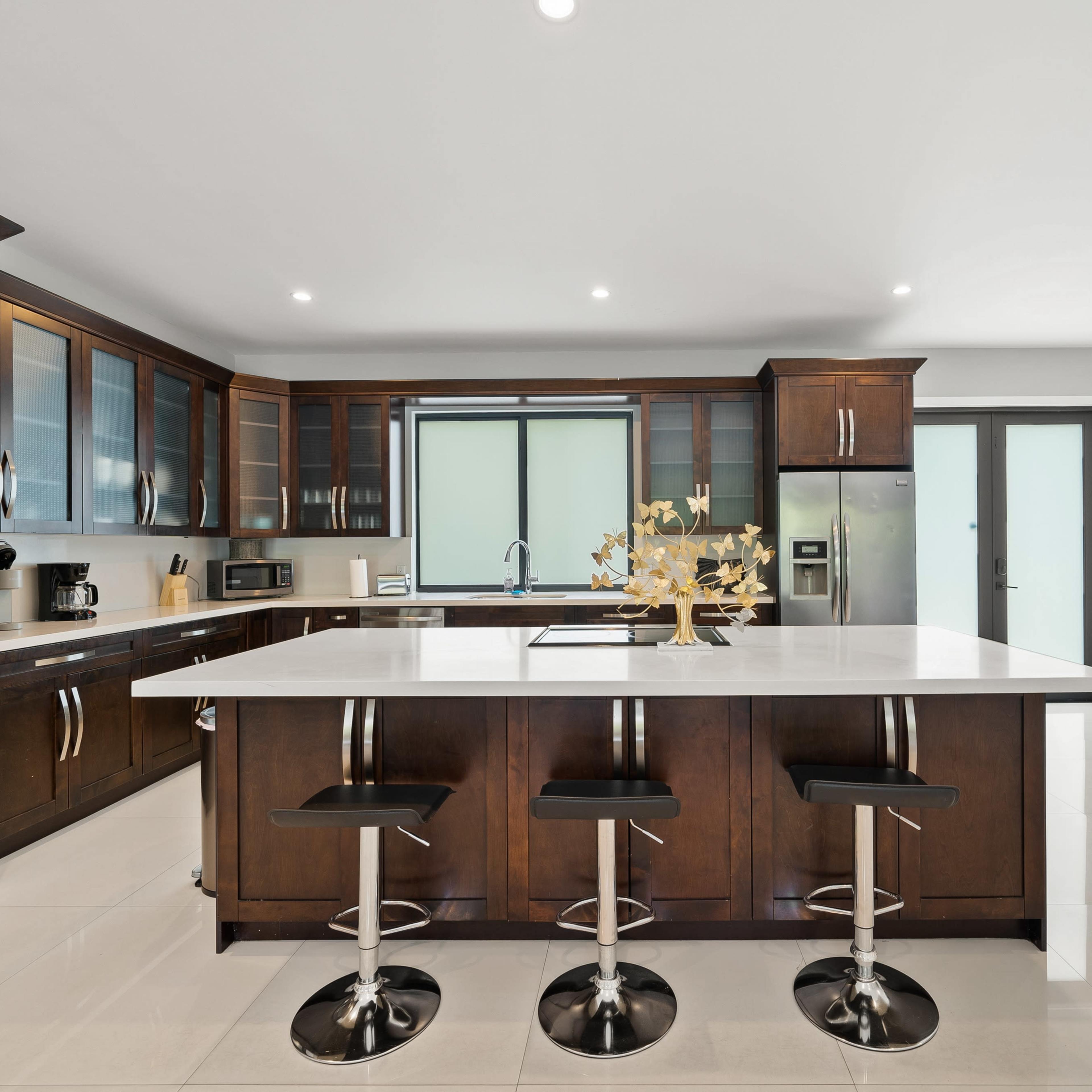The kitchen features dark wooden cabinets, a central island with seating, and modern stainless steel appliances.